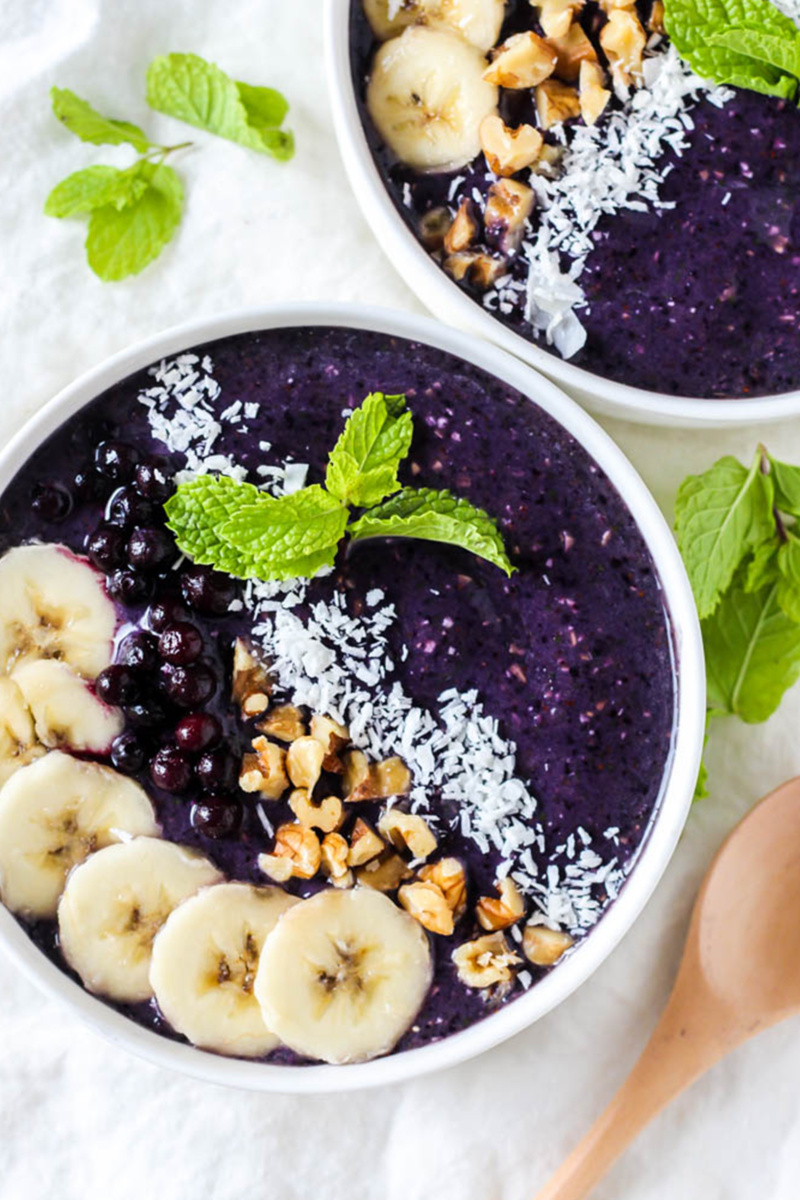 a blueberry smoothie bowl topped with mint, coconut, nuts and sliced bananas