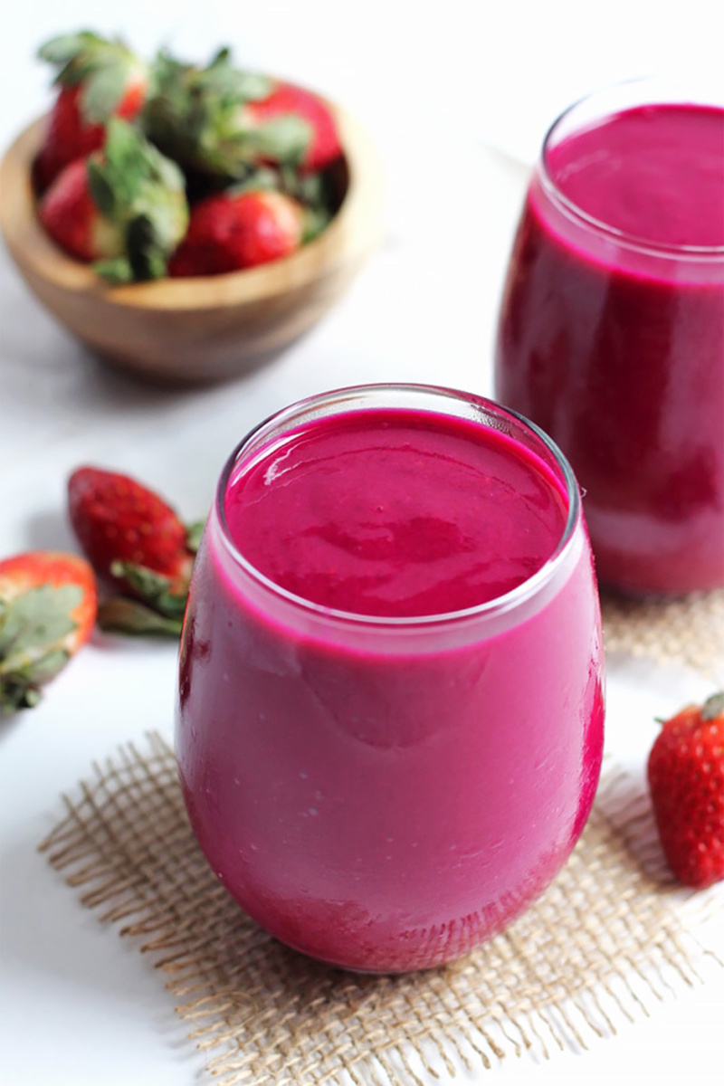 a berry beet smoothie next to a cup of strawberries