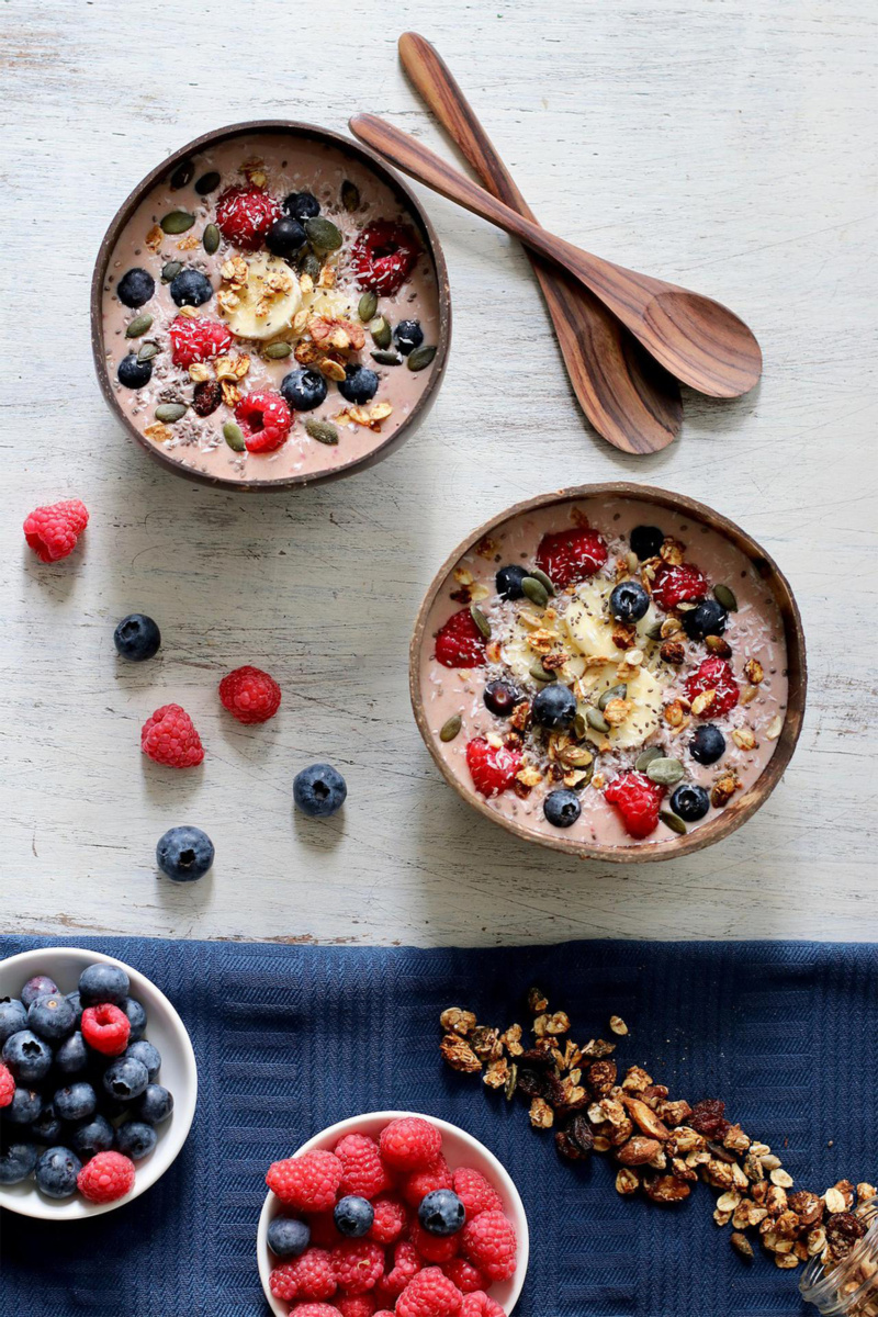 two bowls of peanut butter and berry smoothie bowl topped with fresh berries, seeds and sliced banana