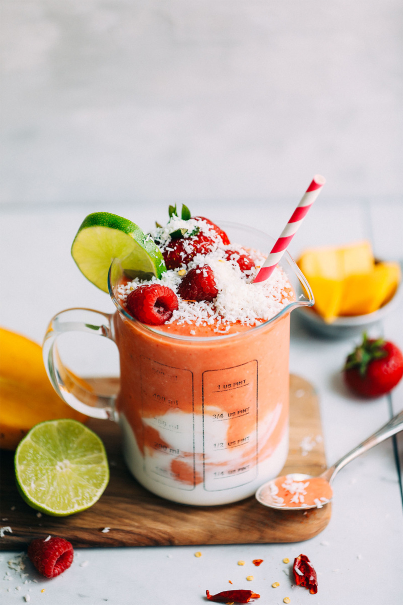 a berry smoothie with coconut cream topped with fresh coconut, berries and a slice of lime