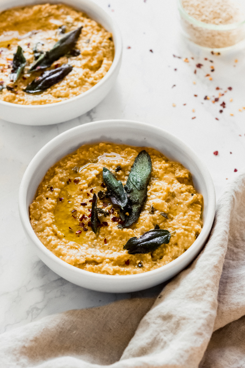 two bowls of pumpkin oat risotto topped with fried sage and chili flakes