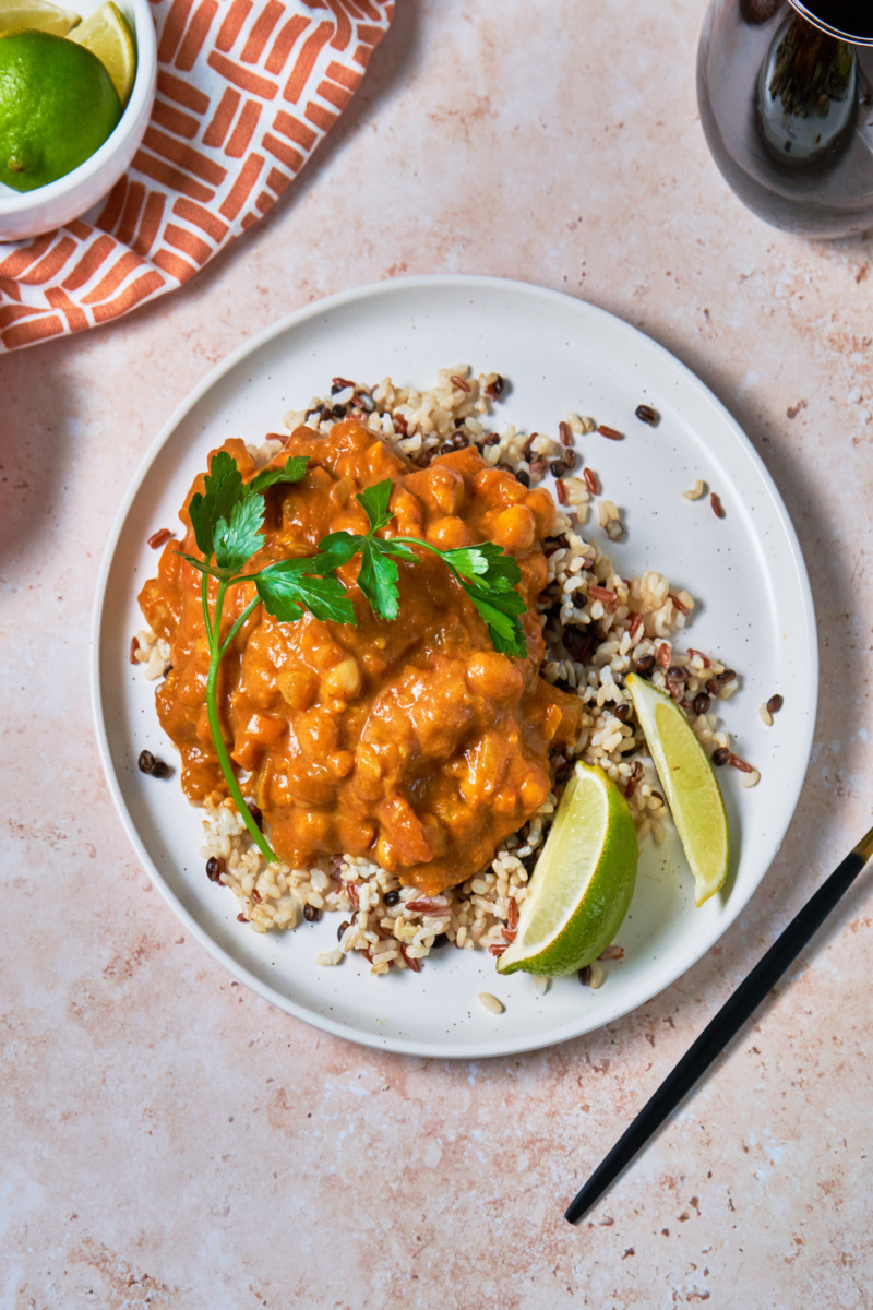 a plate of pumpkin curry served over a bed of mixed grains and topped with cilantro and lime wedges