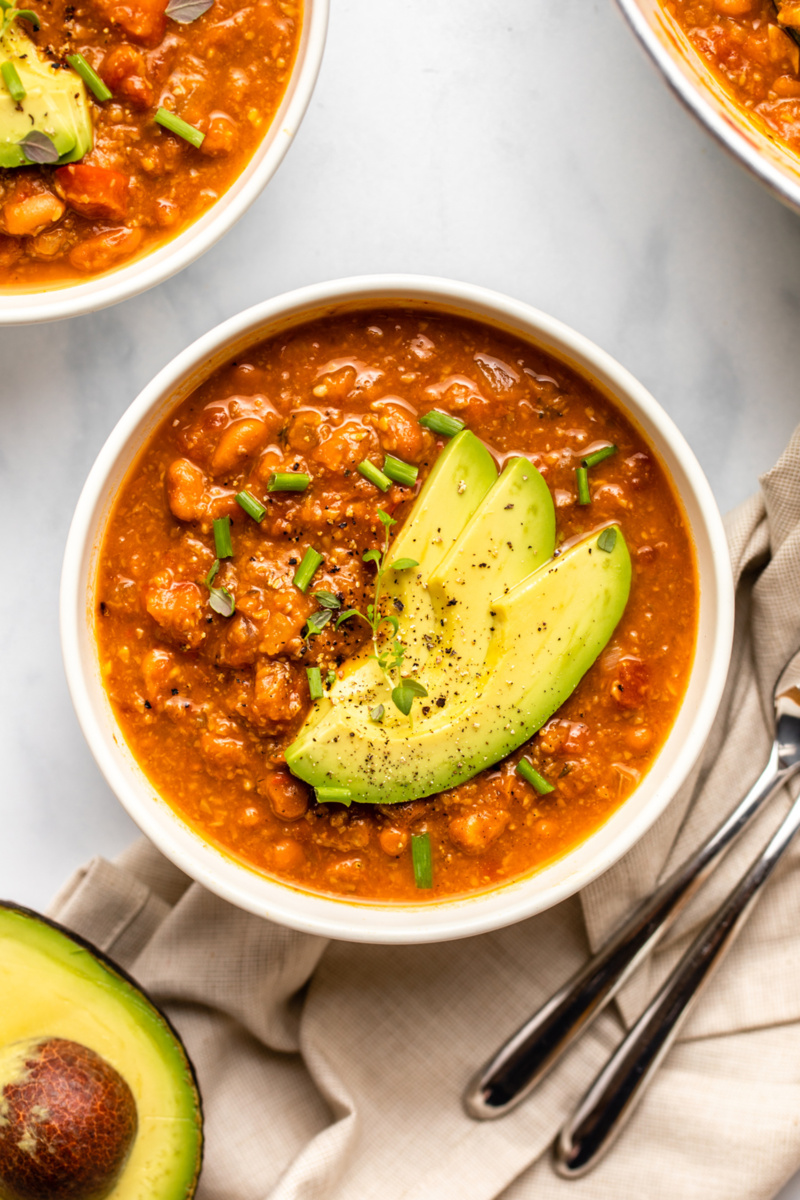 a bowl of vegan pumpkin chili topped with avocado slices and fresh herbs