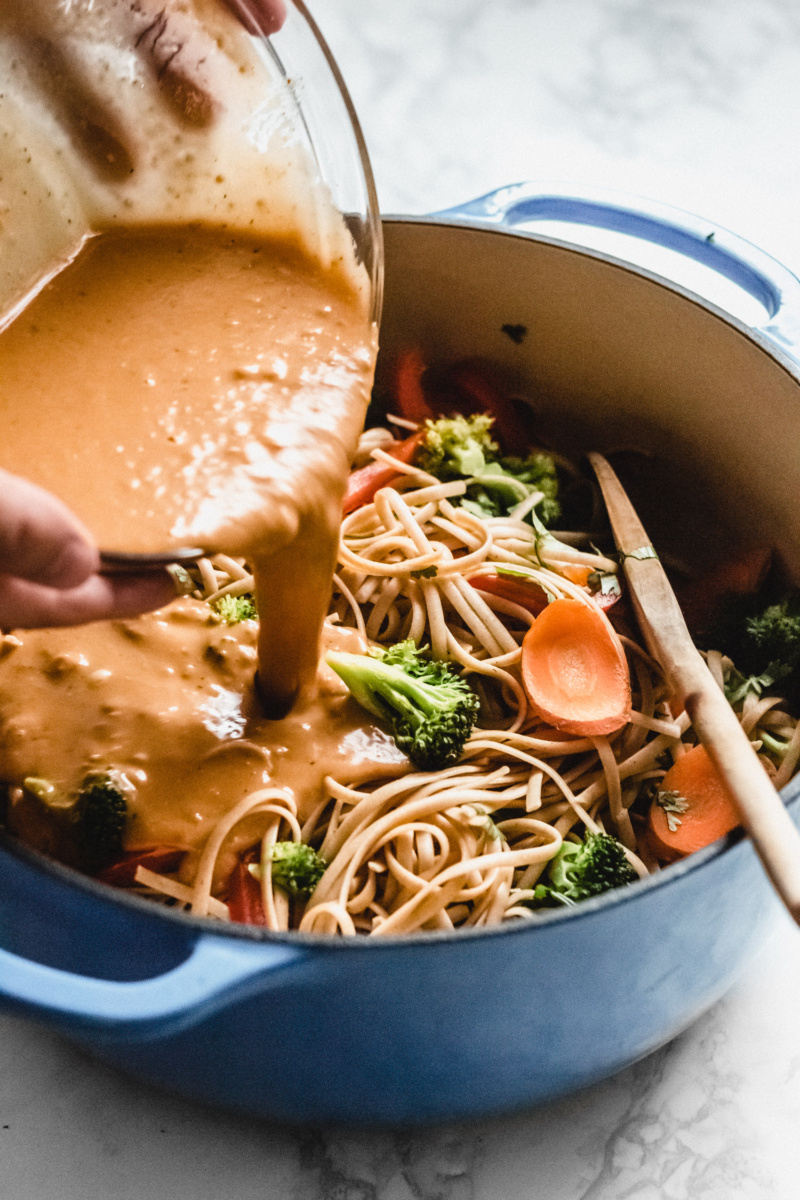 a pot of stir fried noodles being topped with a peanut dressing