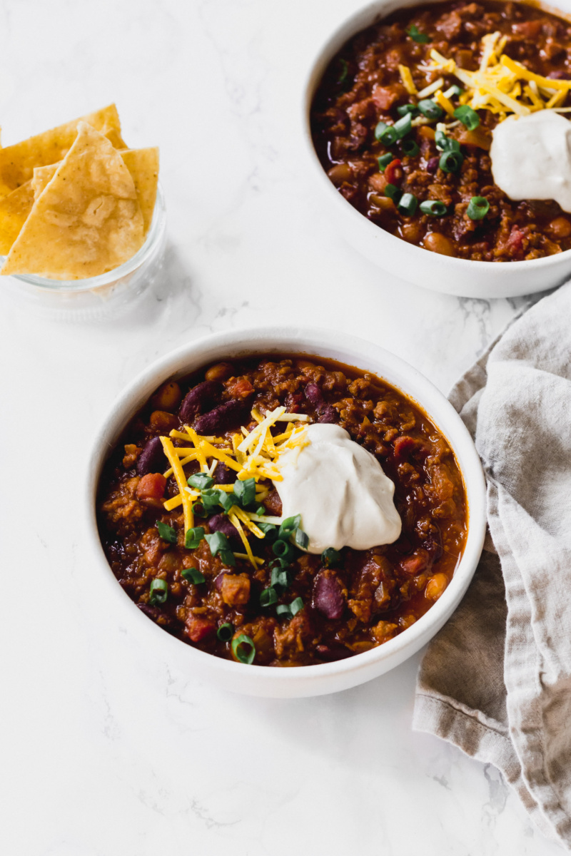 two bowls of chili, each topped with sour cream, shredded cheese and green onions