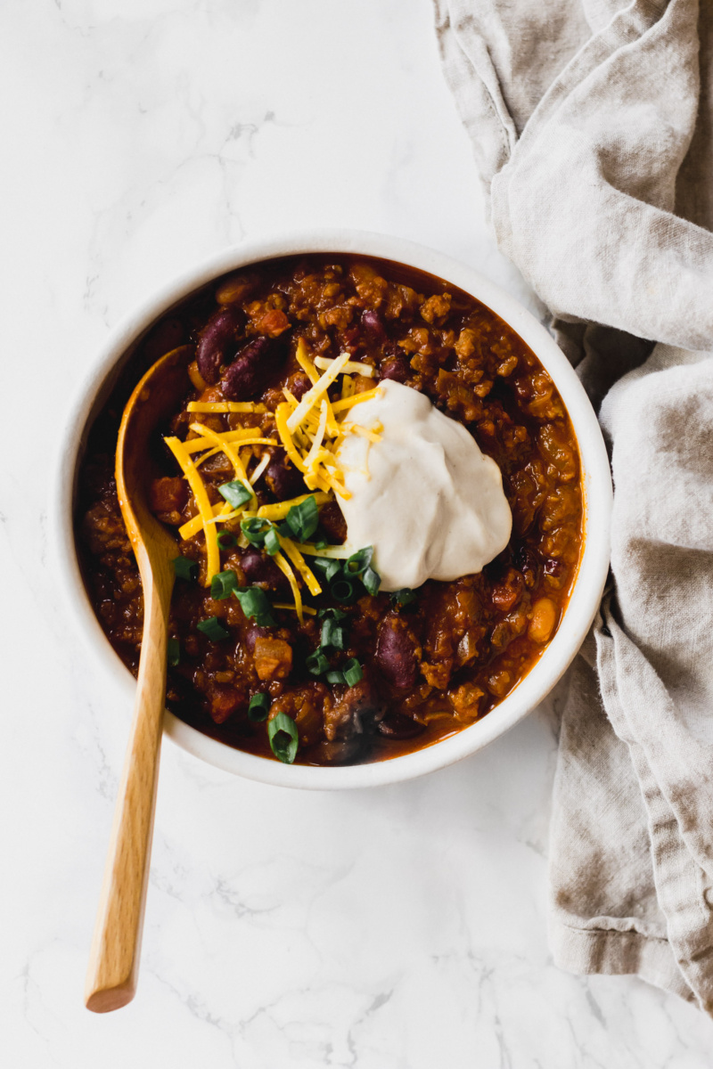 a bowl of vegan chili served with sour cream, shredded vegan cheese and sliced green onion