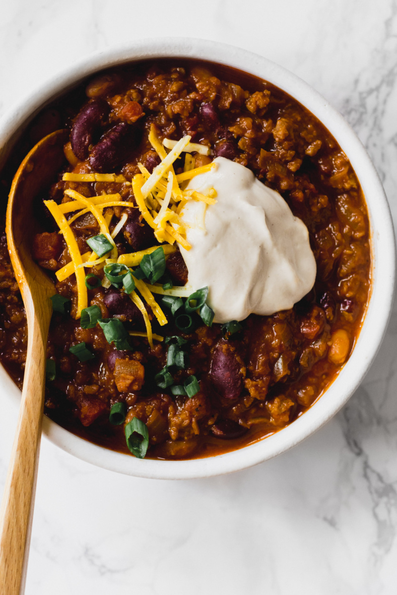 a wooden spoon taking a scoop out of a bowl of vegan chili