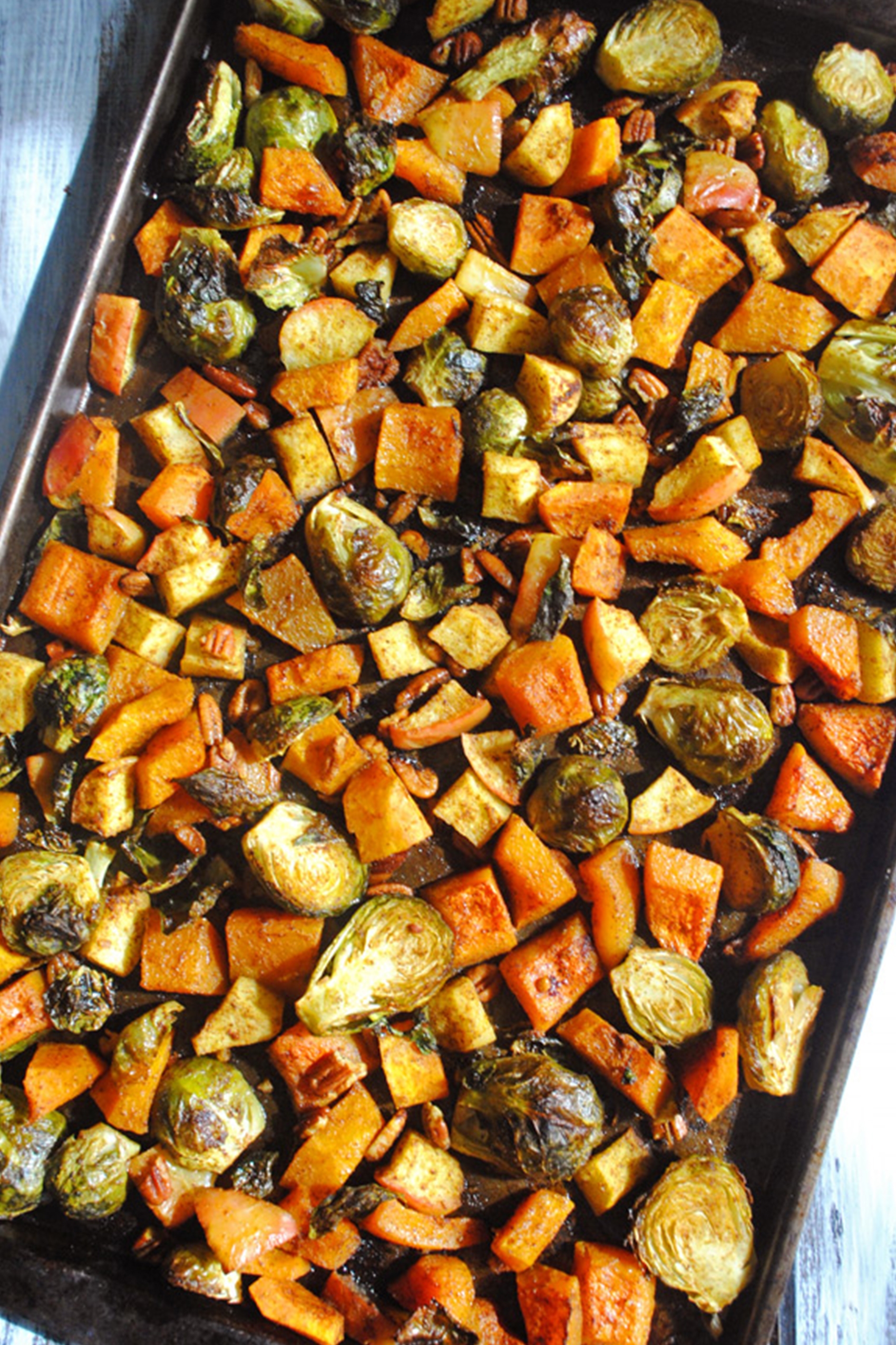 a sheet tray of roasted vegetables including brussels sprouts, squash, apples and pecans