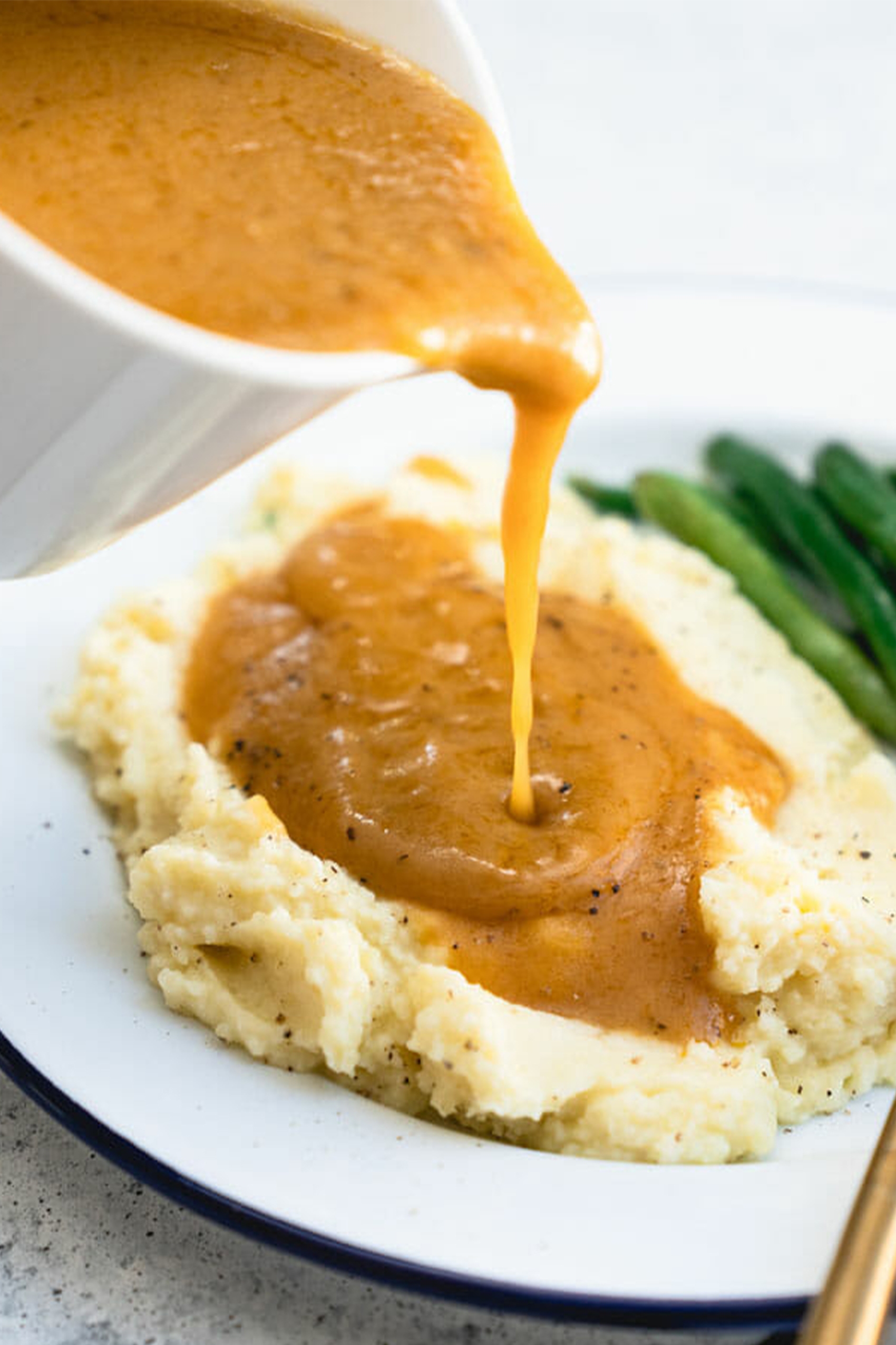 a boat of vegan gravy being poured over mashed potatoes