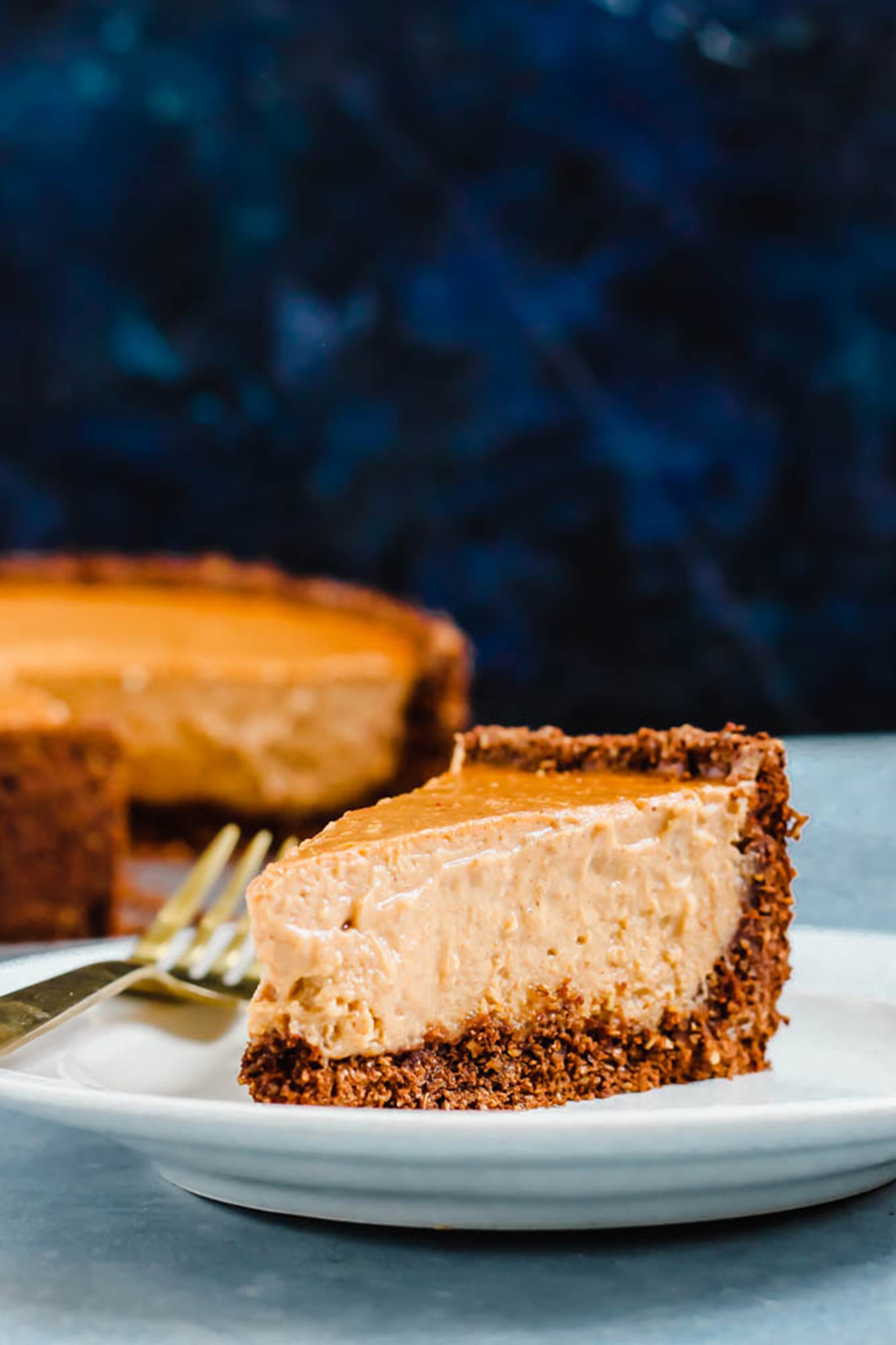 a slice of vegan pumpkin cheesecake sitting in front of the whole cheesecake
