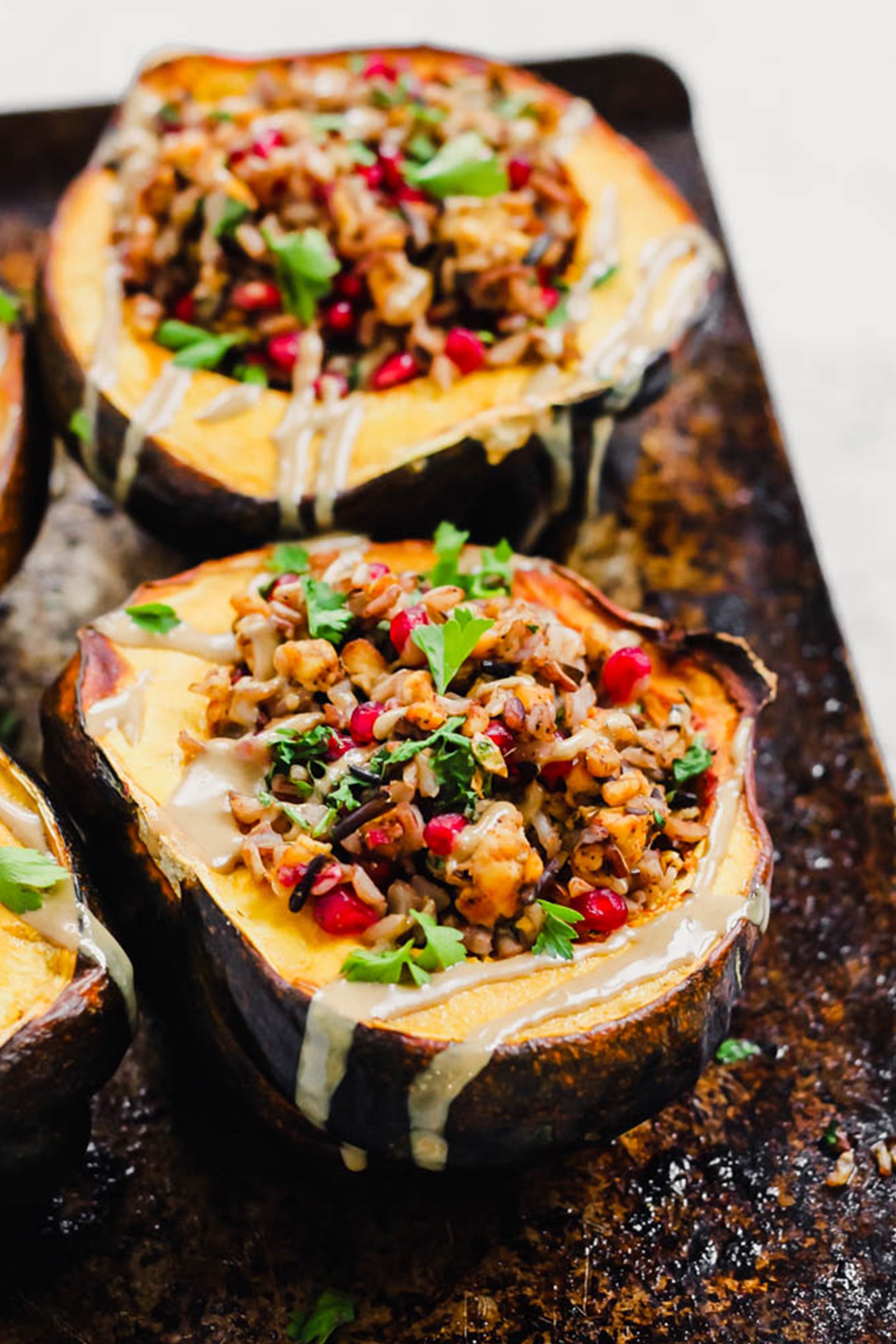 acorn squashes filled with a tempeh and wild rice stuffing topped with pomegranate seeds and tahini