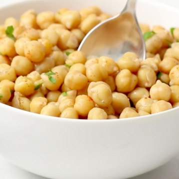 A spoon taking a scoop of cooked chickpeas from a bowl