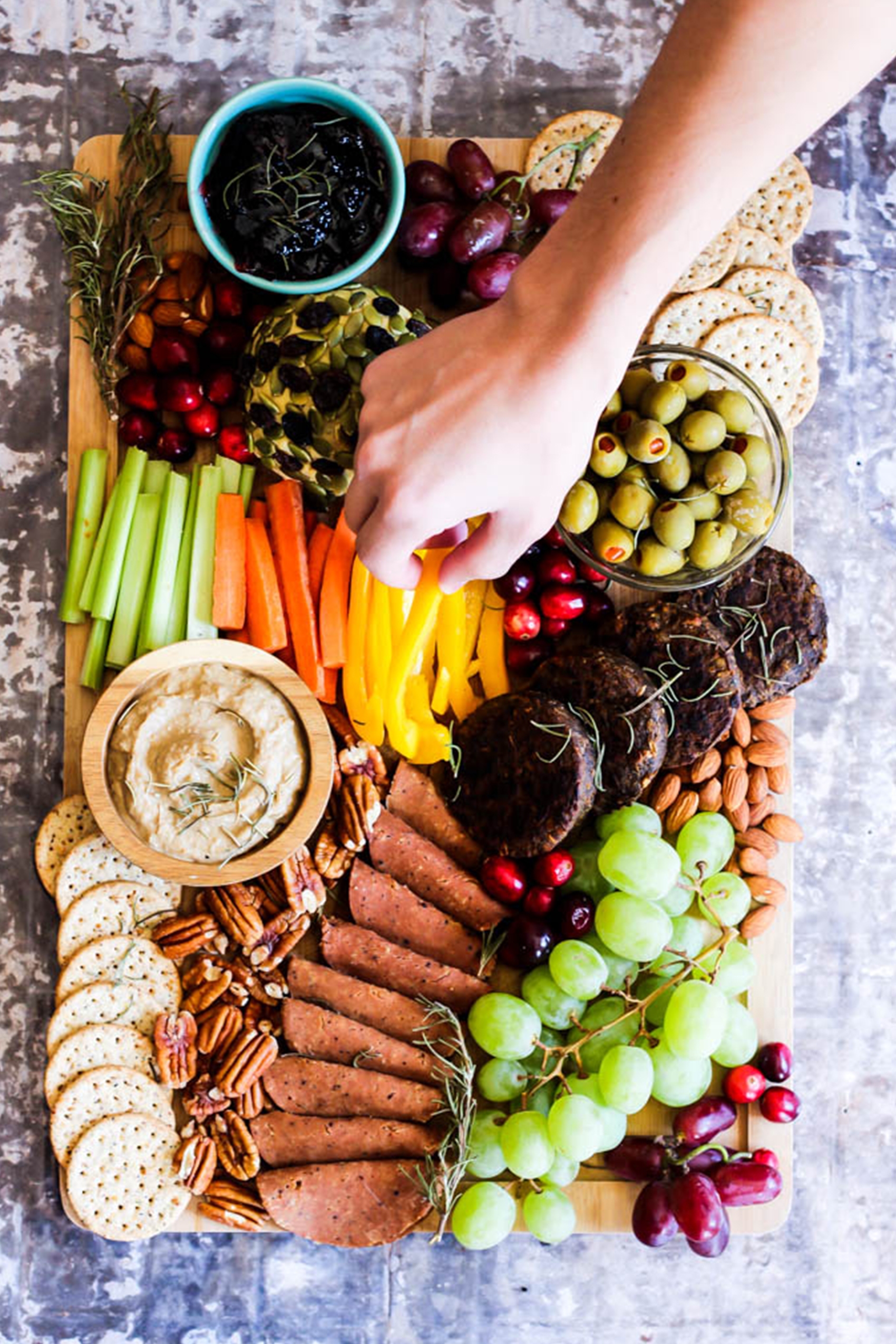 a hand grabbing a sliced pepper from a charcuterie board