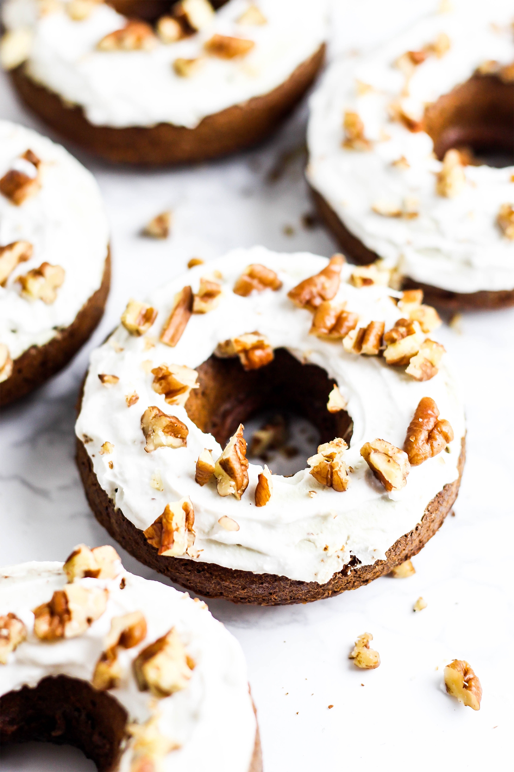 a batch of gingerbread donuts topped with whipped coconut cream and pecans