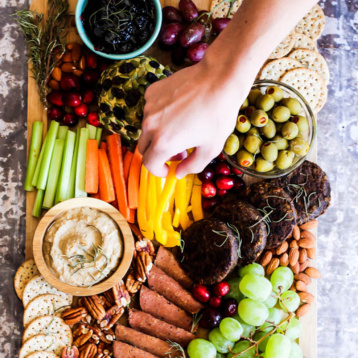 a hand reaching for a sliced pepper on a snack board