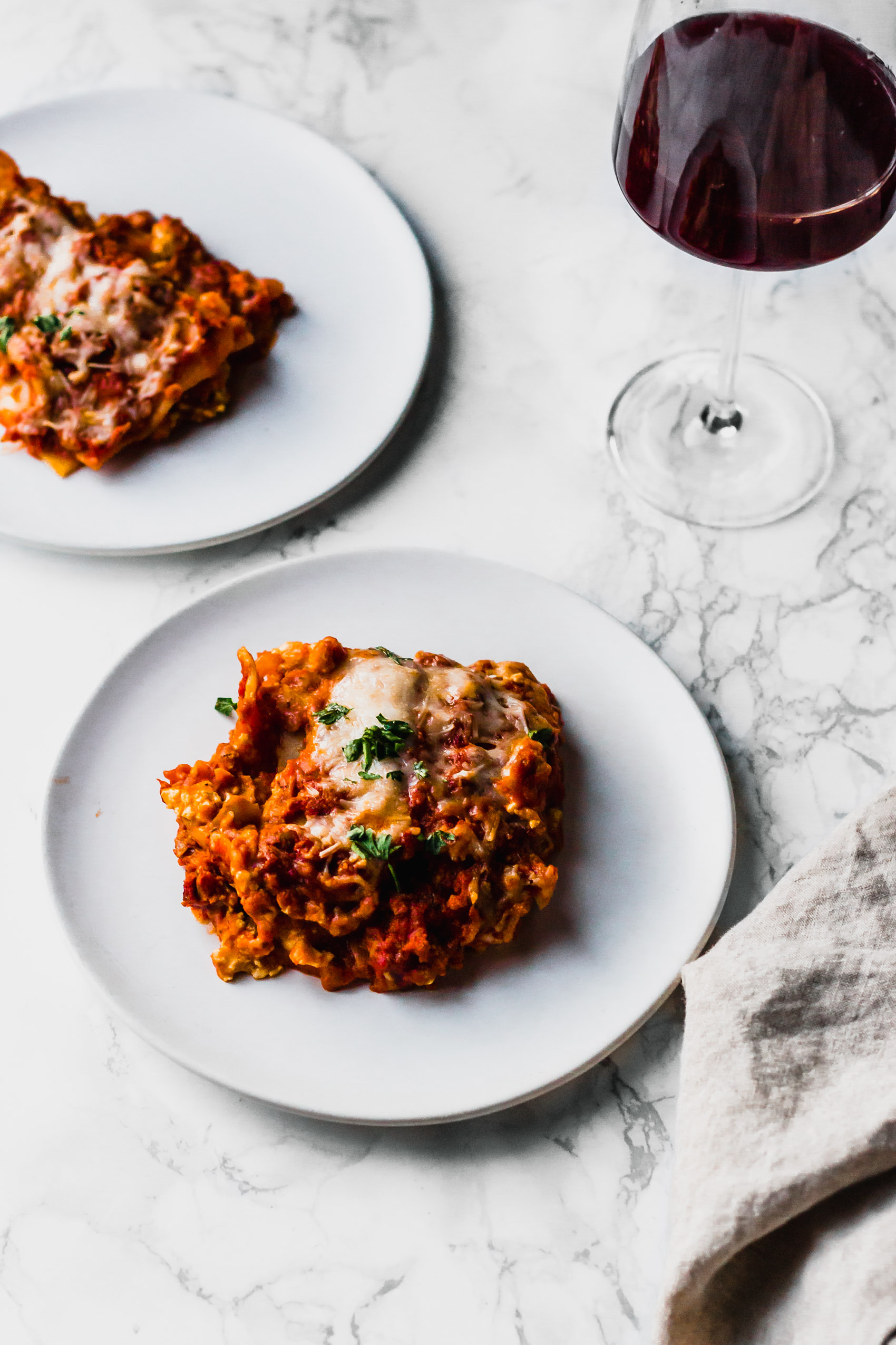 two plates of plant based lasagna next to a glass of red wine