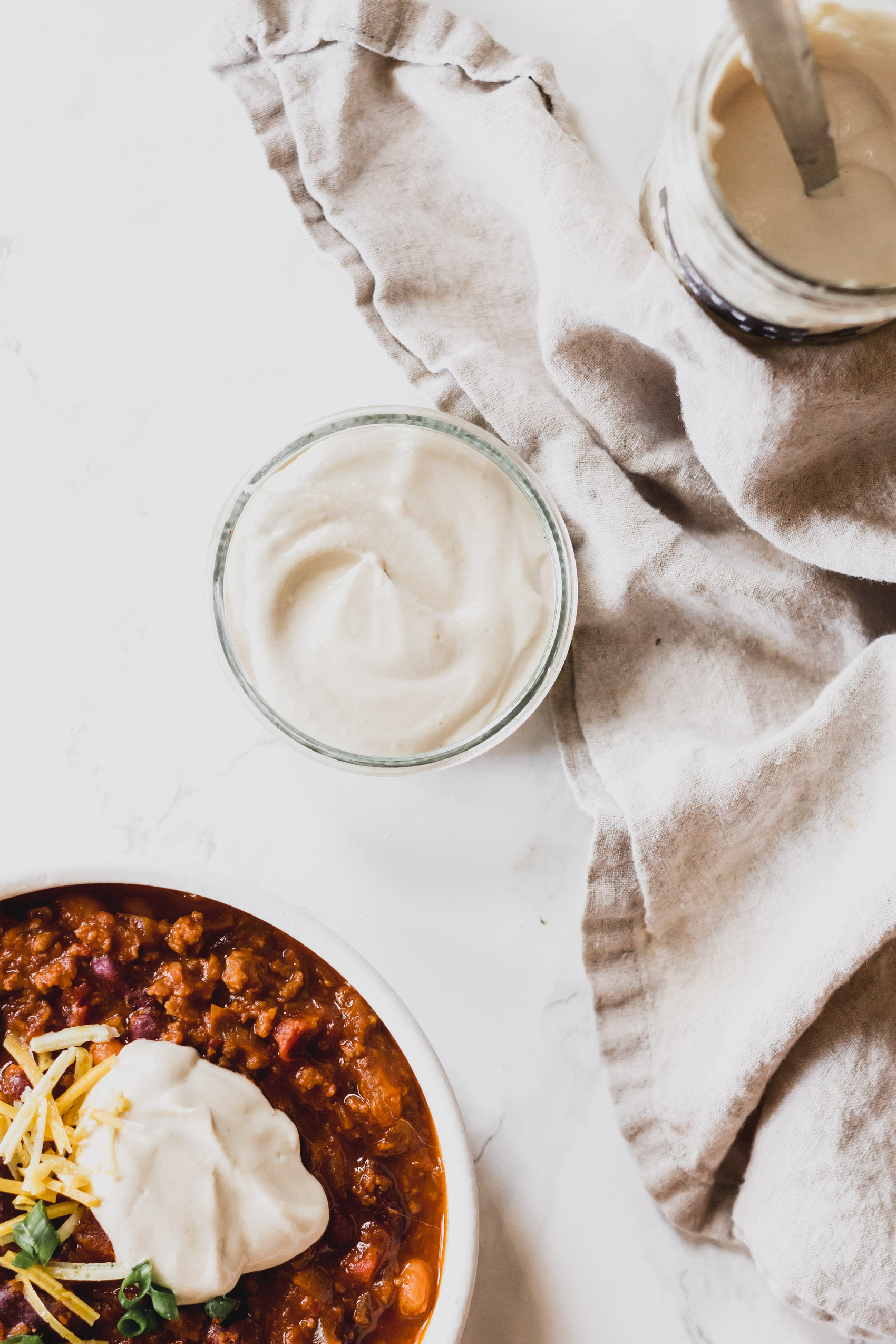 a small bowl of vegan sour cream next to a bowl of chili