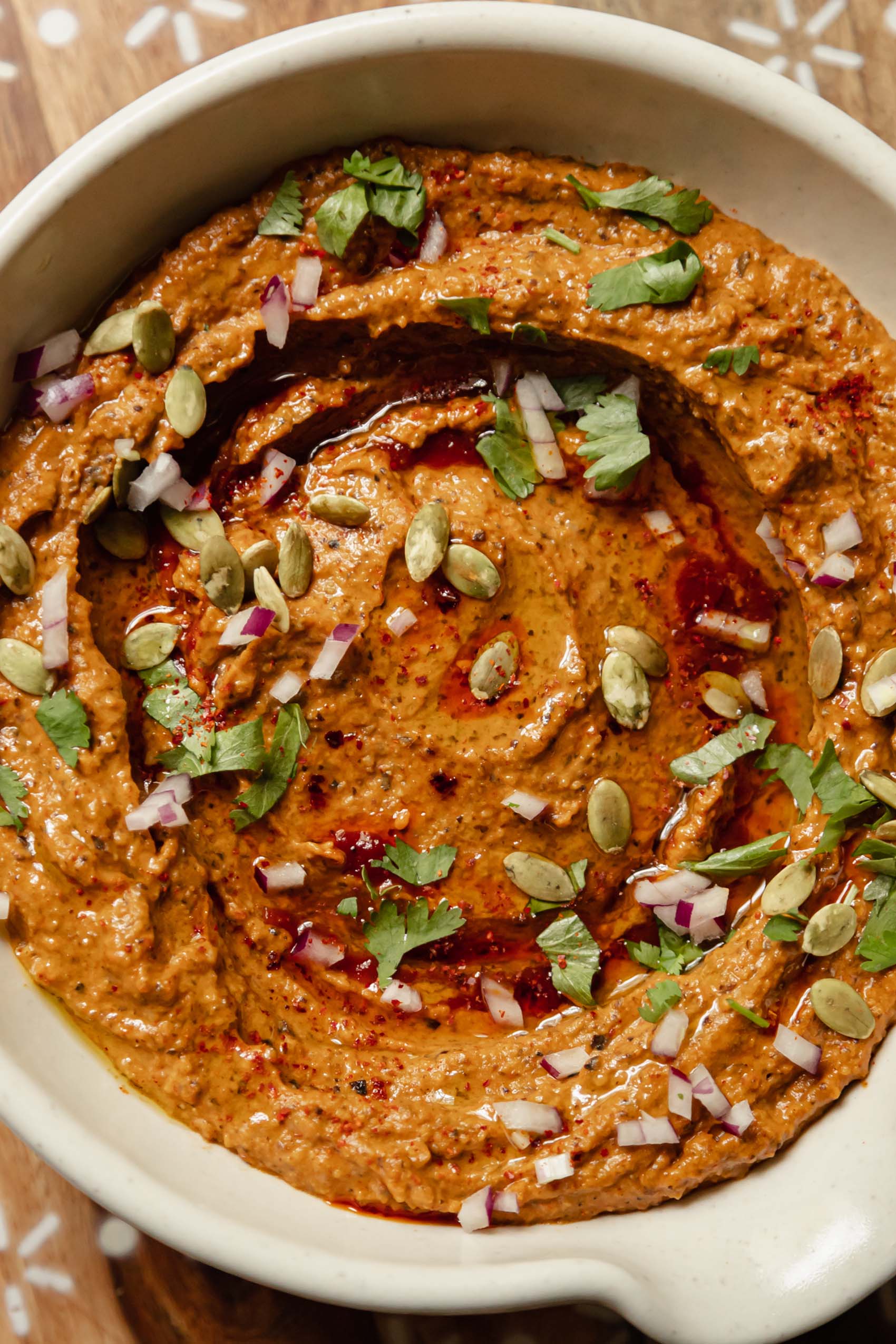 a bowl of black bean dip topped with cilantro, diced red onion and pepitas