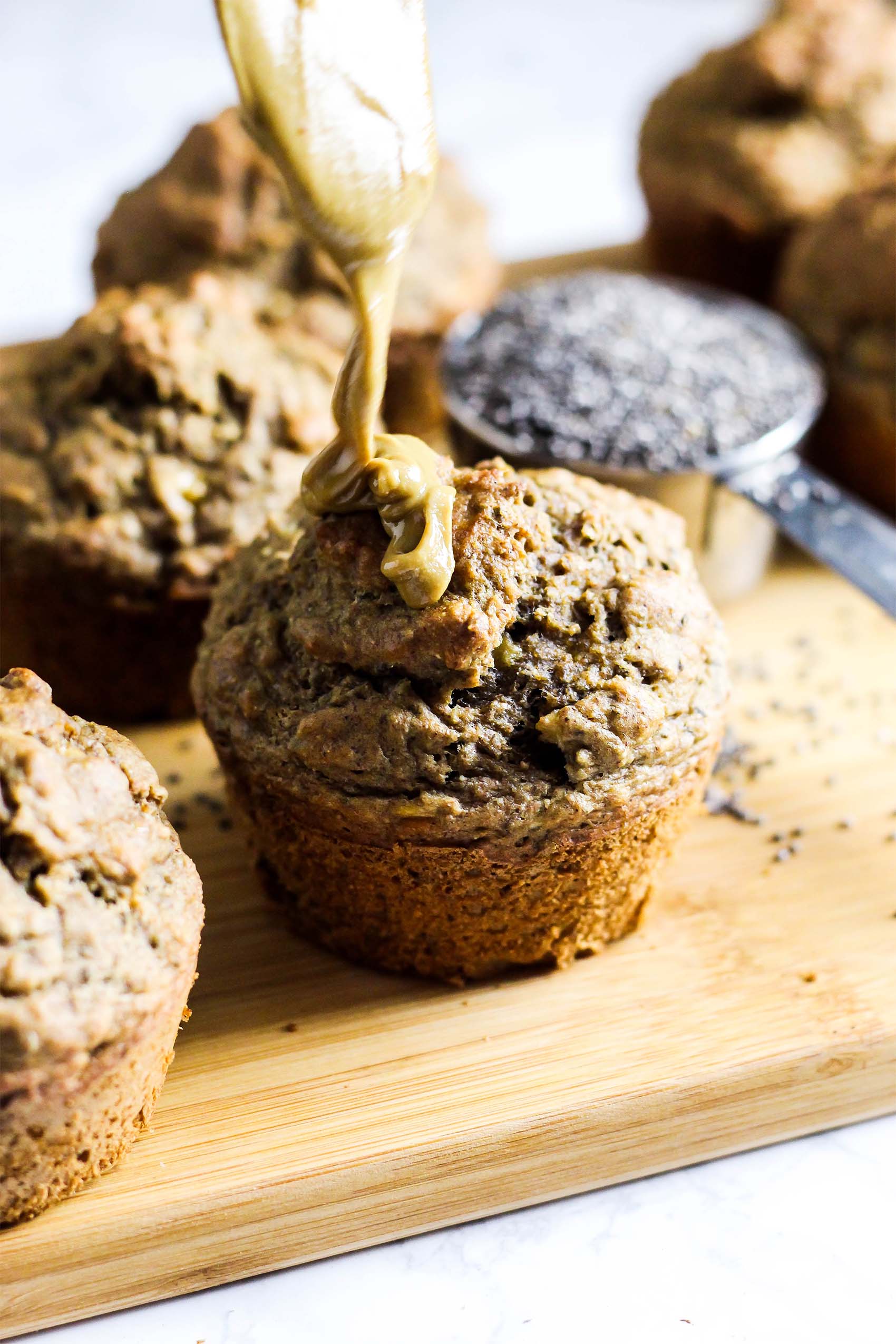 a batch of banana chia almond butter muffins being drizzled with almond butter