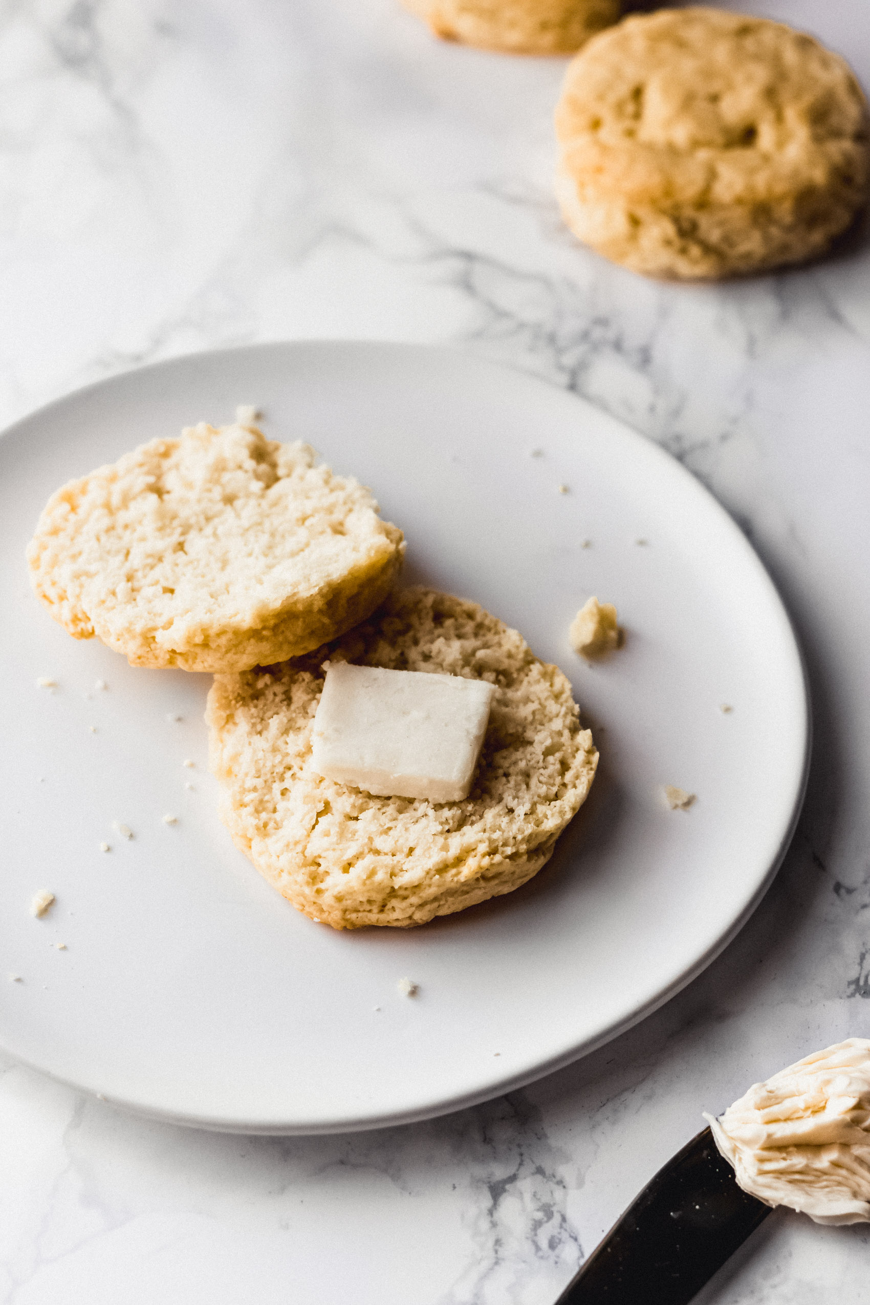 a vegan biscuit sliced in half and topped with a pat of butter