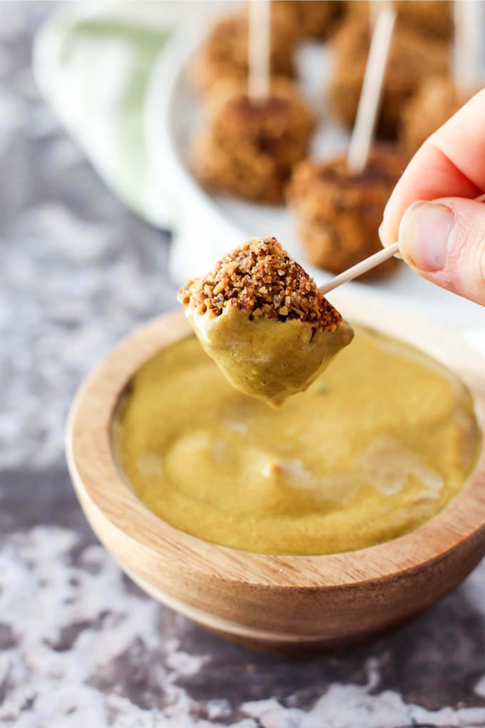 a tofu nugget being dipped into a cup of honey mustard