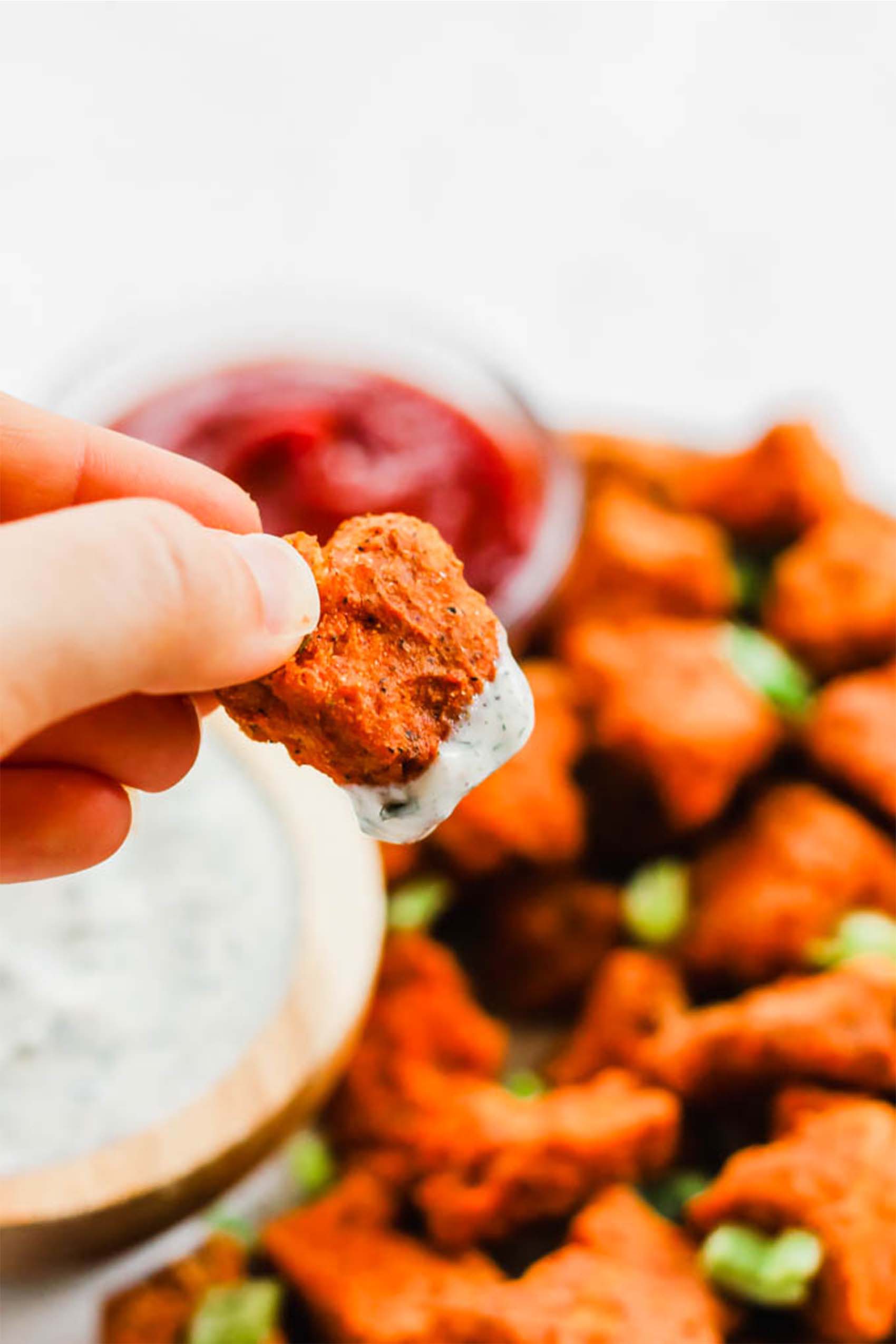 a hand holding a buffalo tofu nugget dipped in dairy free ranch