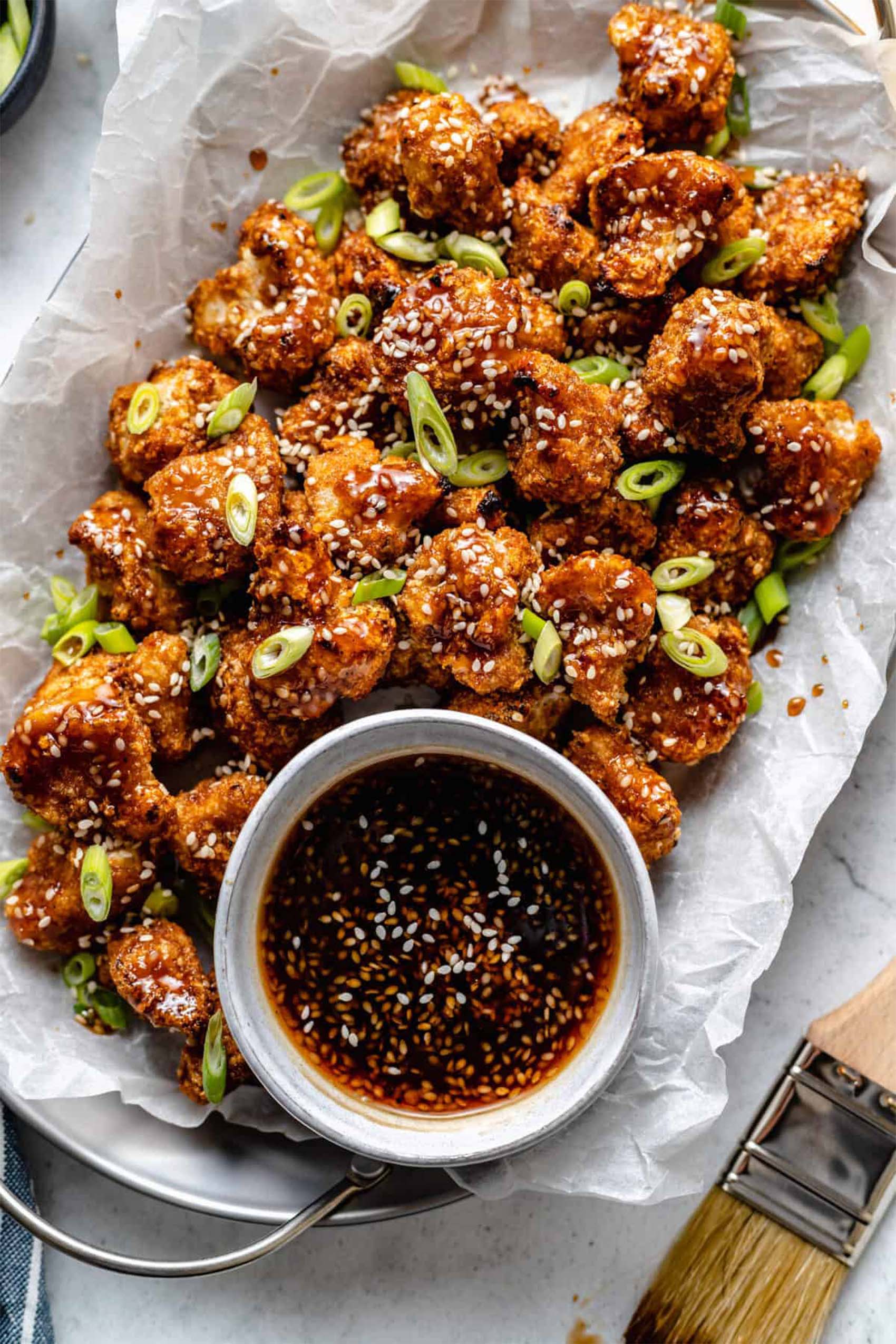 a platter of vegan sticky sesame cauliflower wings served with dipping sauce