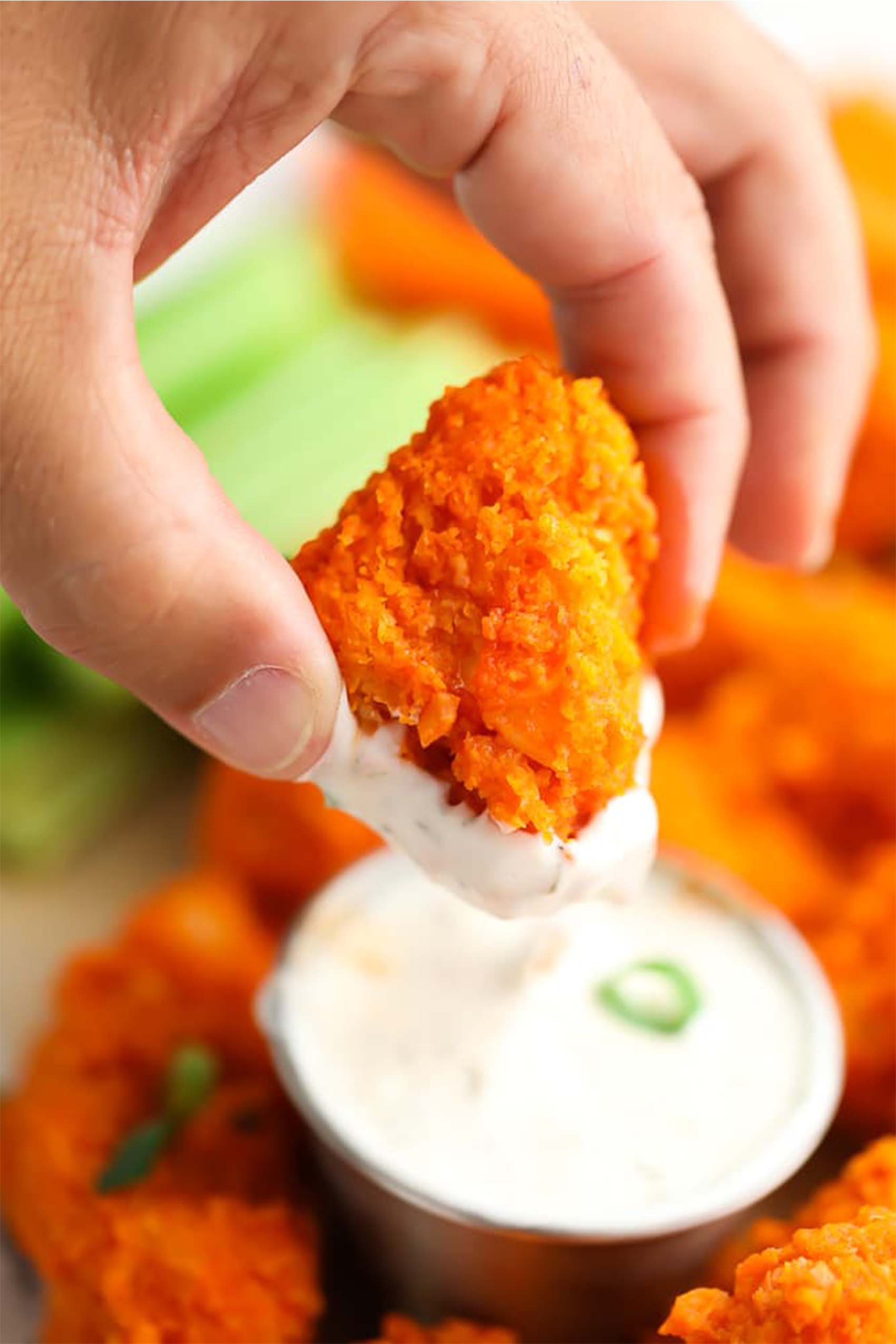 a hand dipping a buffalo cauliflower wing into a cup of vegan ranch
