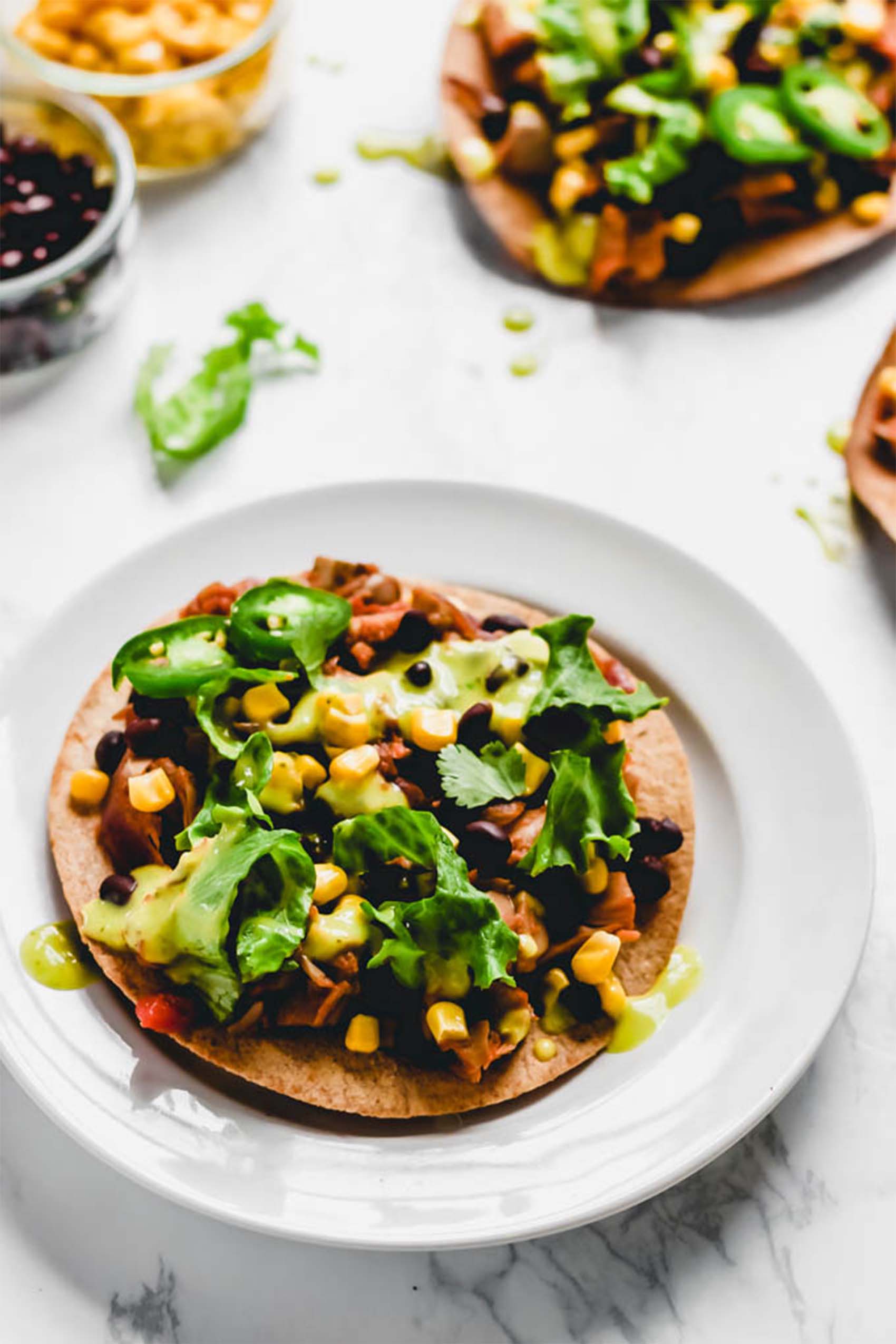 a vegan tostada topped with beans, corn, avocado, cilantro and jalapeno