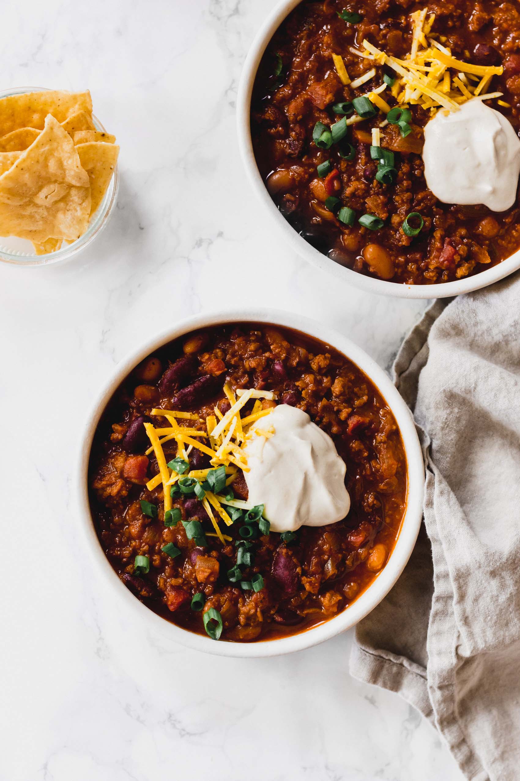 two bowls of vegan chili topped with cheese and vegan sour cream