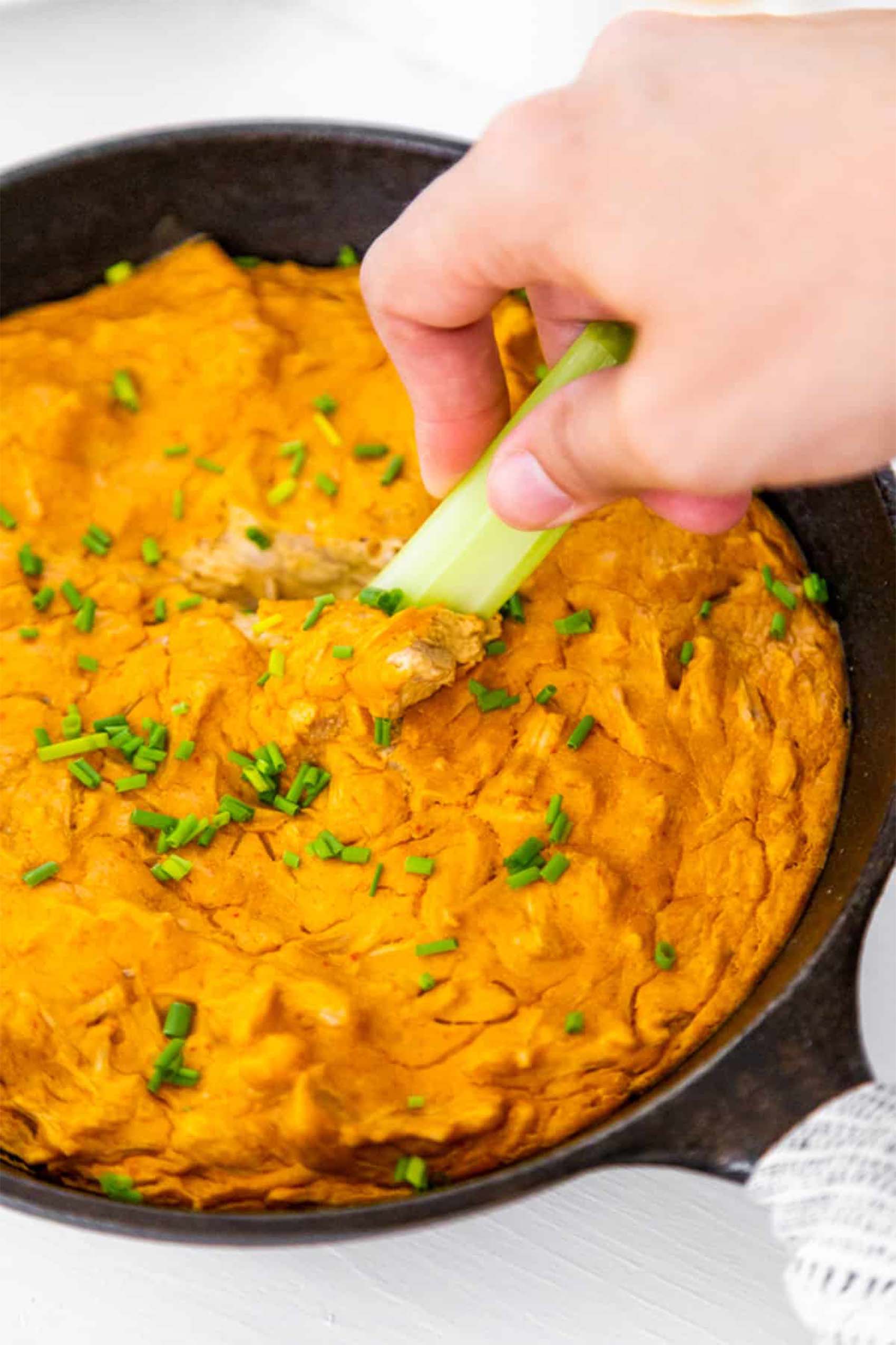 a piece of celery being dipped into a pan of vegan buffalo chicken dip