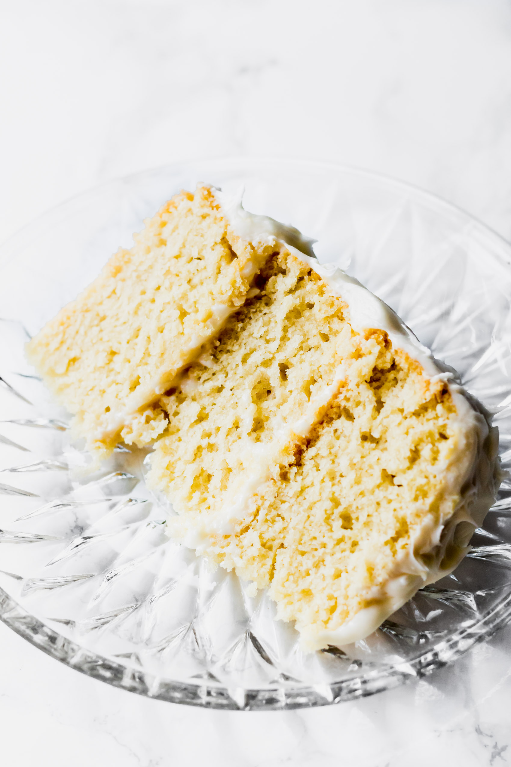 a slice of three layer vanilla cake served on a glass plate