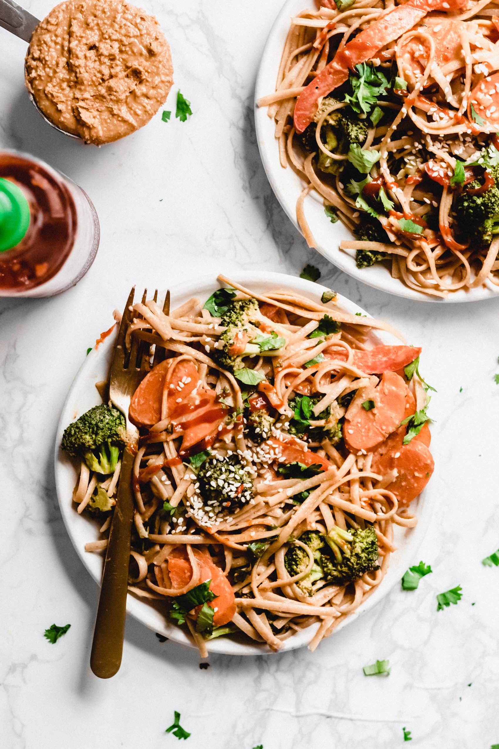 two plates of peanut butter noodles served with hot sauce