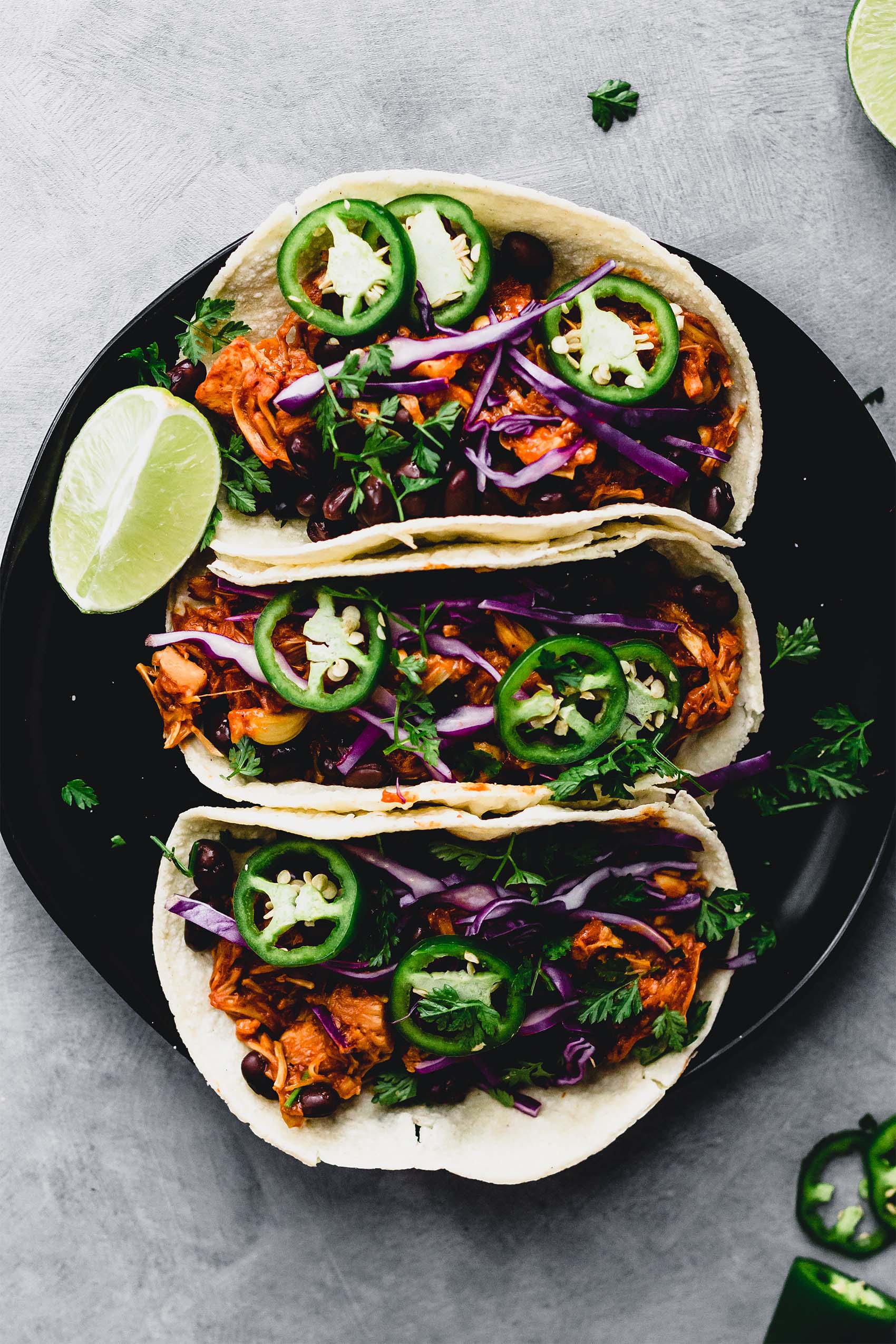 a plate of three bbq vegan tacos topped with sliced jalapenos and served with a lime wedge