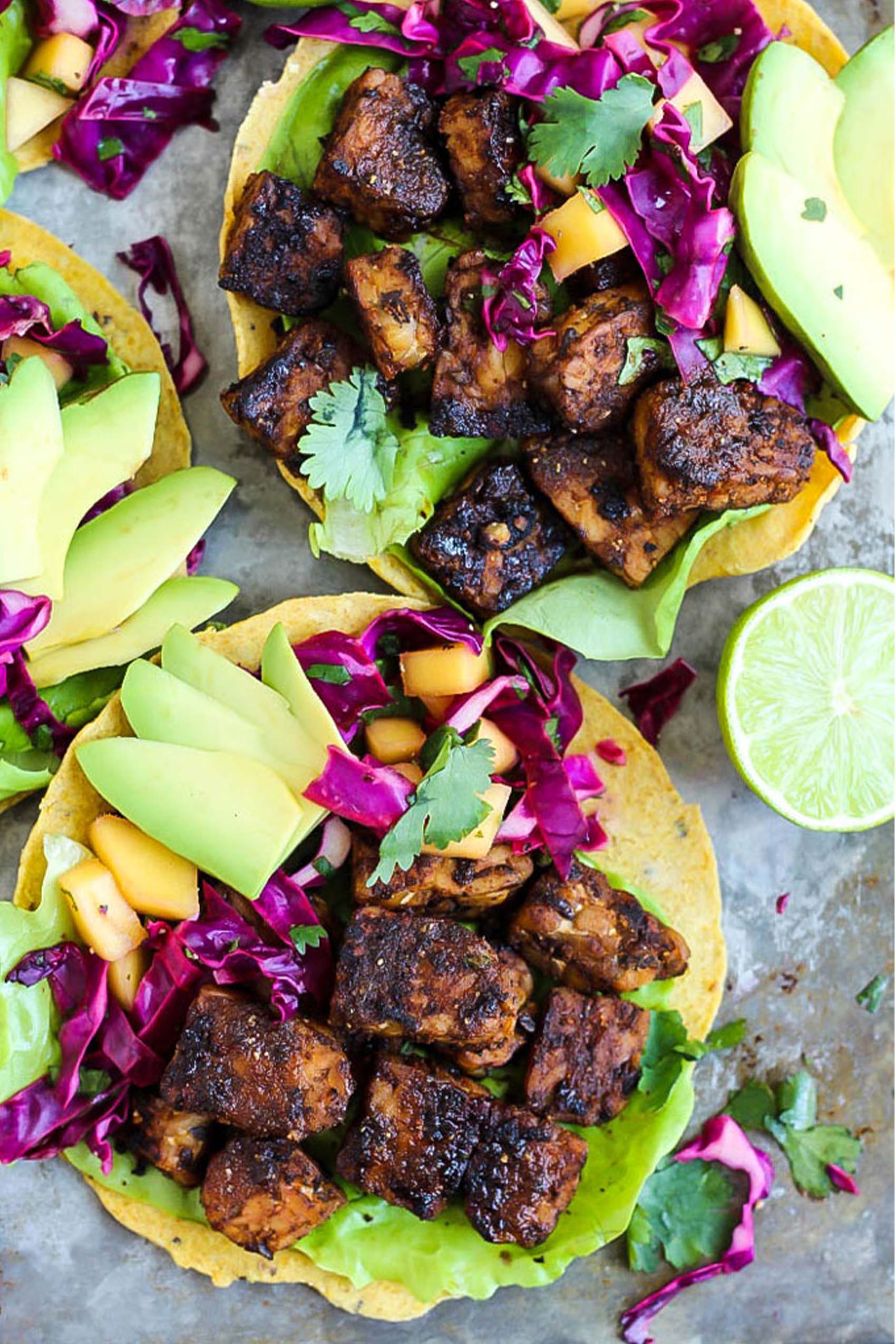 three tempeh tostadas topped with avocado slices and mango cabbage slaw