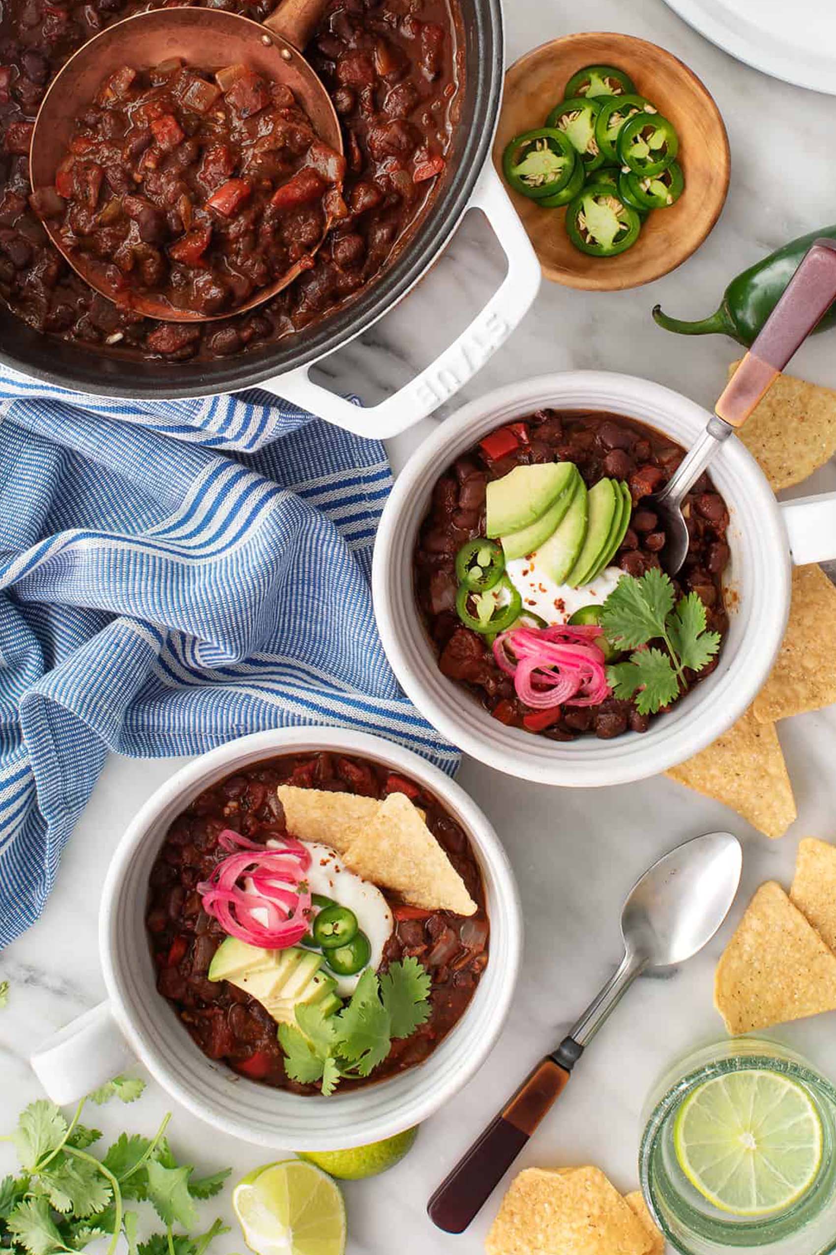 two bowls of black bean chili, each topped with avocado, pickled onion and fresh herbs