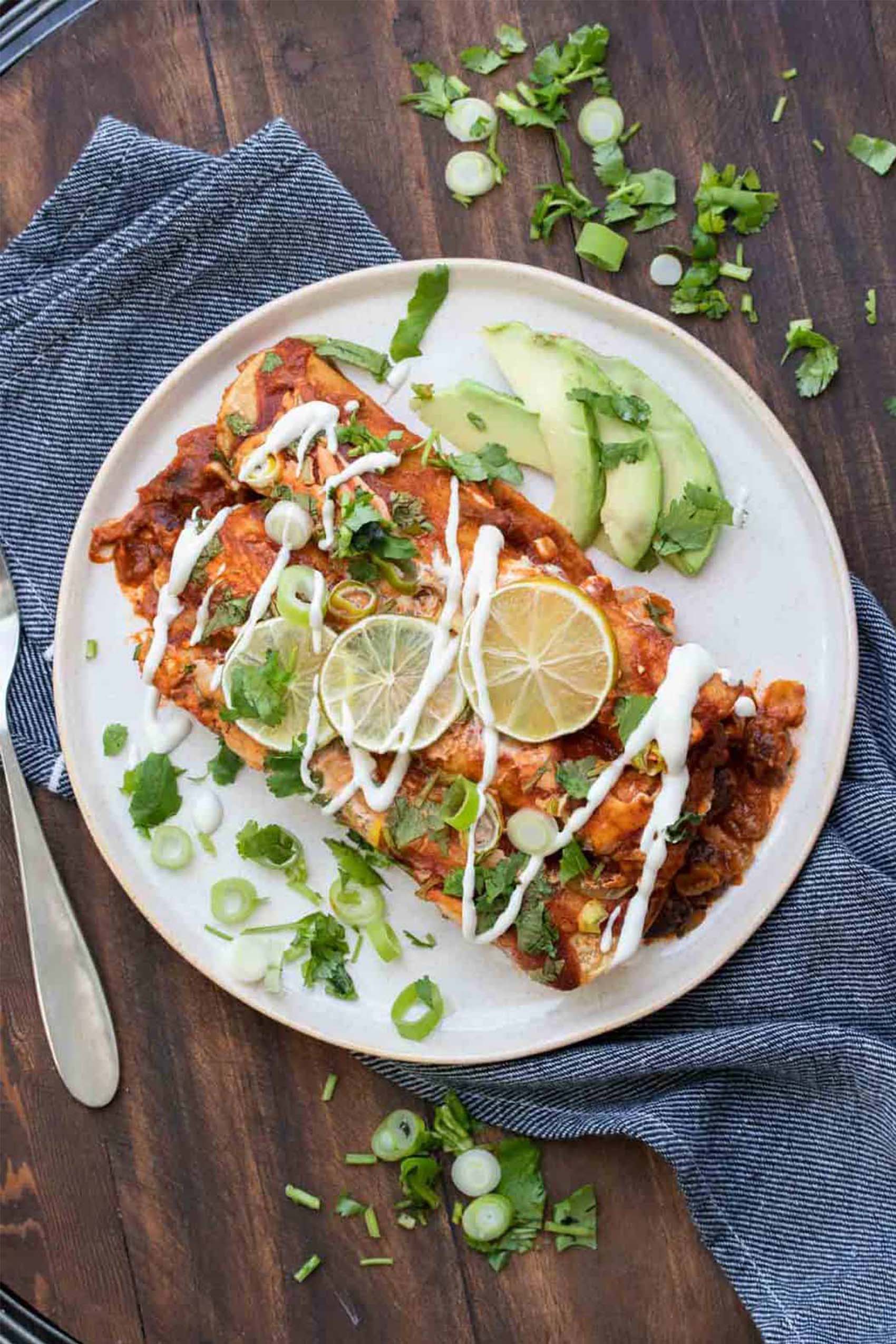 a plate of two black bean enchiladas topped with slices of lime and vegan sour cream