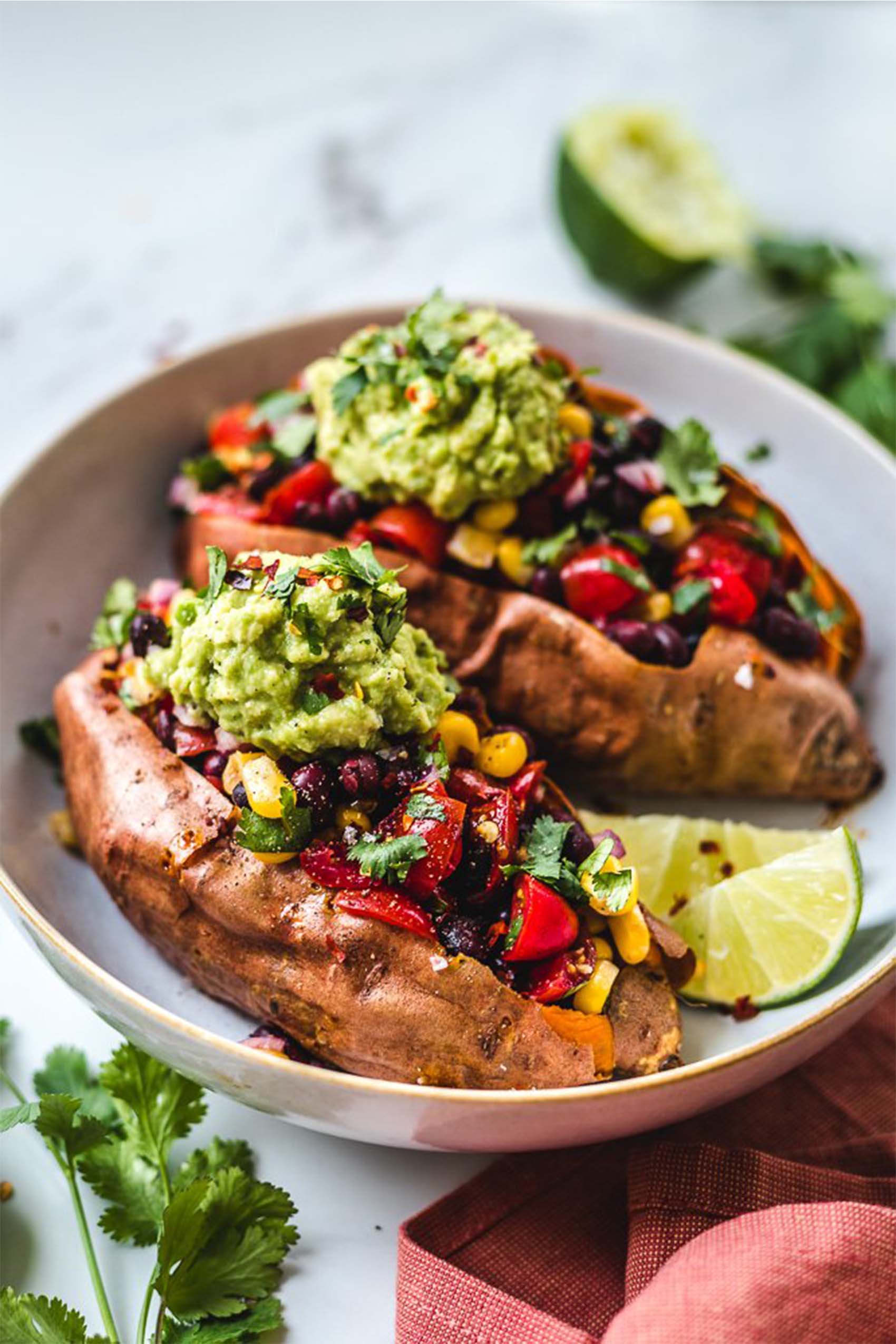 two sweet potatoes stuffed with black beans, veggies and topped with guacamole