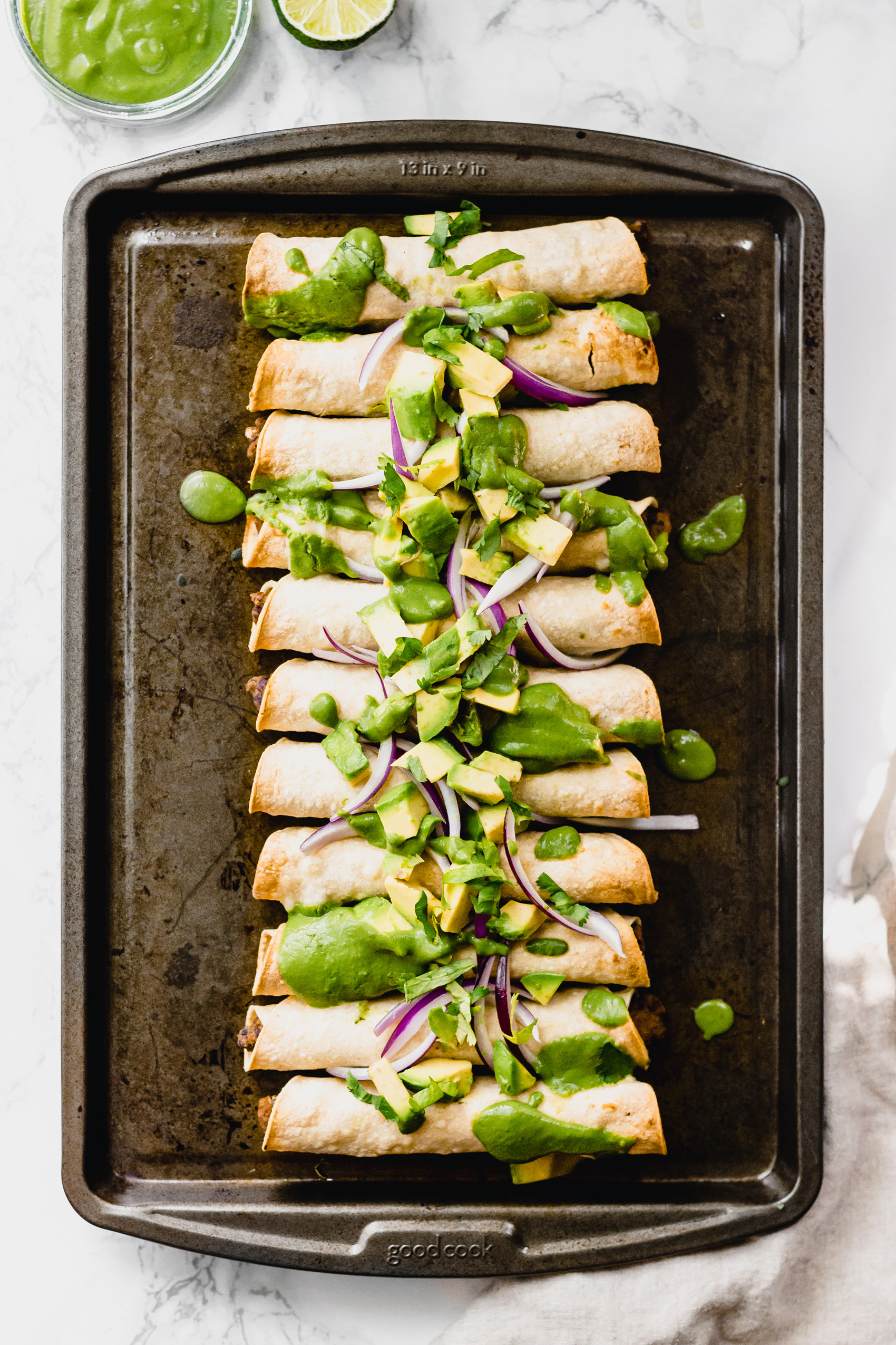 a sheet tray of black bean taquitos topped with sliced red onion, avocados and cilantro