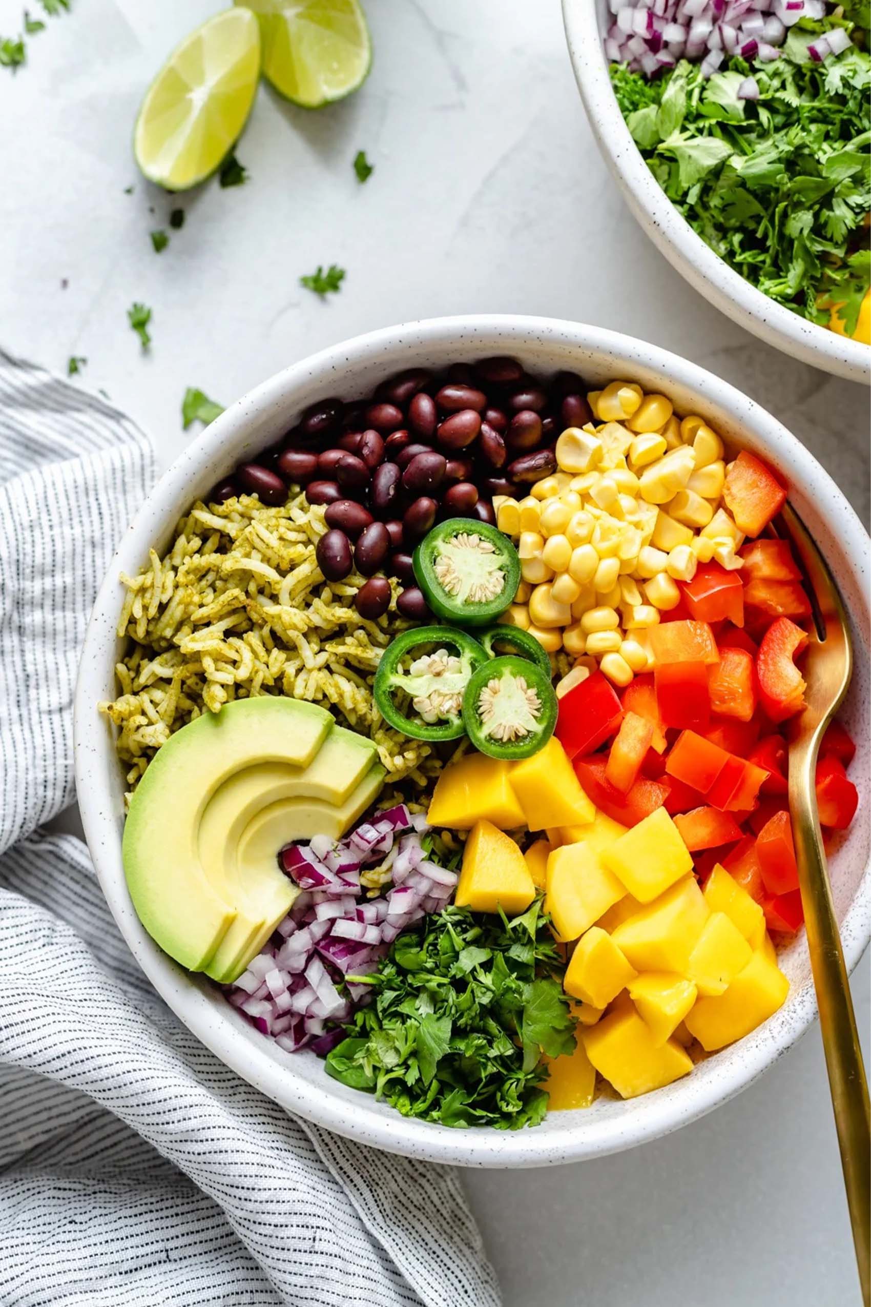 a bowl of rice, corn, black beans, avocado, red onion, cilantro, mango and red bell pepper topped with sliced jalapenos