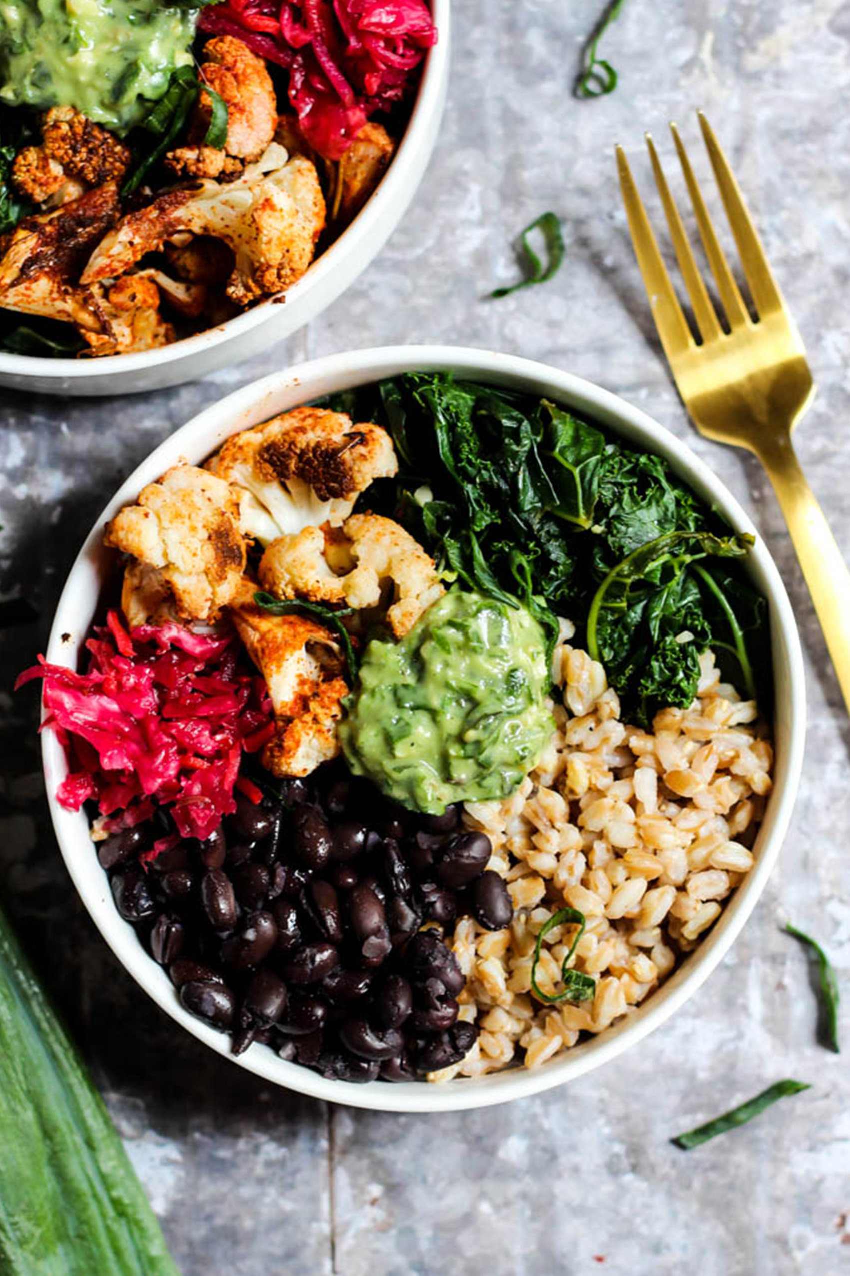a black bean bowl containing brown rice, cabbage slaw, roasted cauliflower, greens and avocado pesto