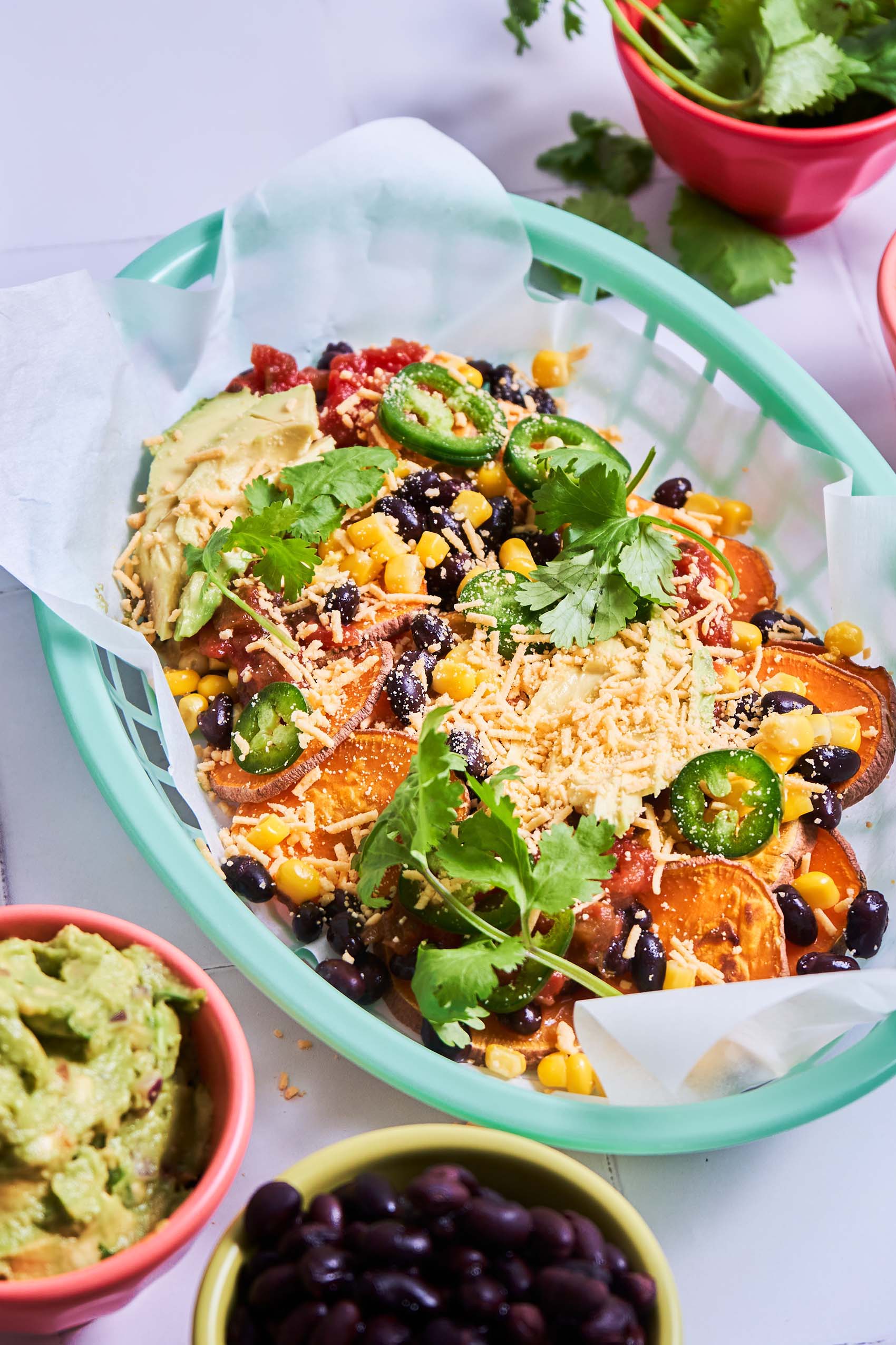 a teal basket filled with sweet potato nachos topped with fresh jalapeno slices and cilantro
