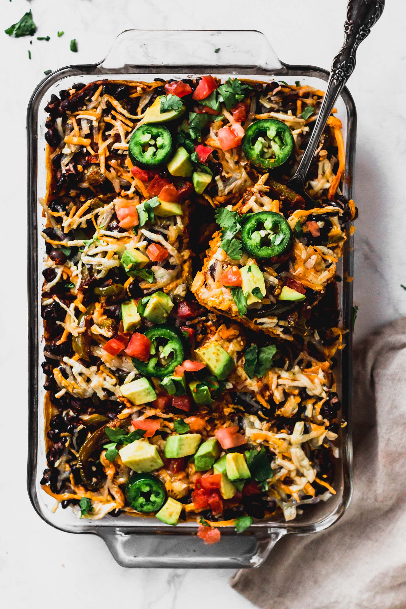 a casserole dish containing a black bean enchilada casserole topped with fresh avocado and jalapeno slices