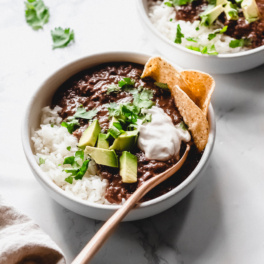 two bowls of black bean soup topped with sliced avocado and cilantro