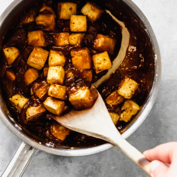 a pot of teriyaki tofu being stirred with a wooden spoon