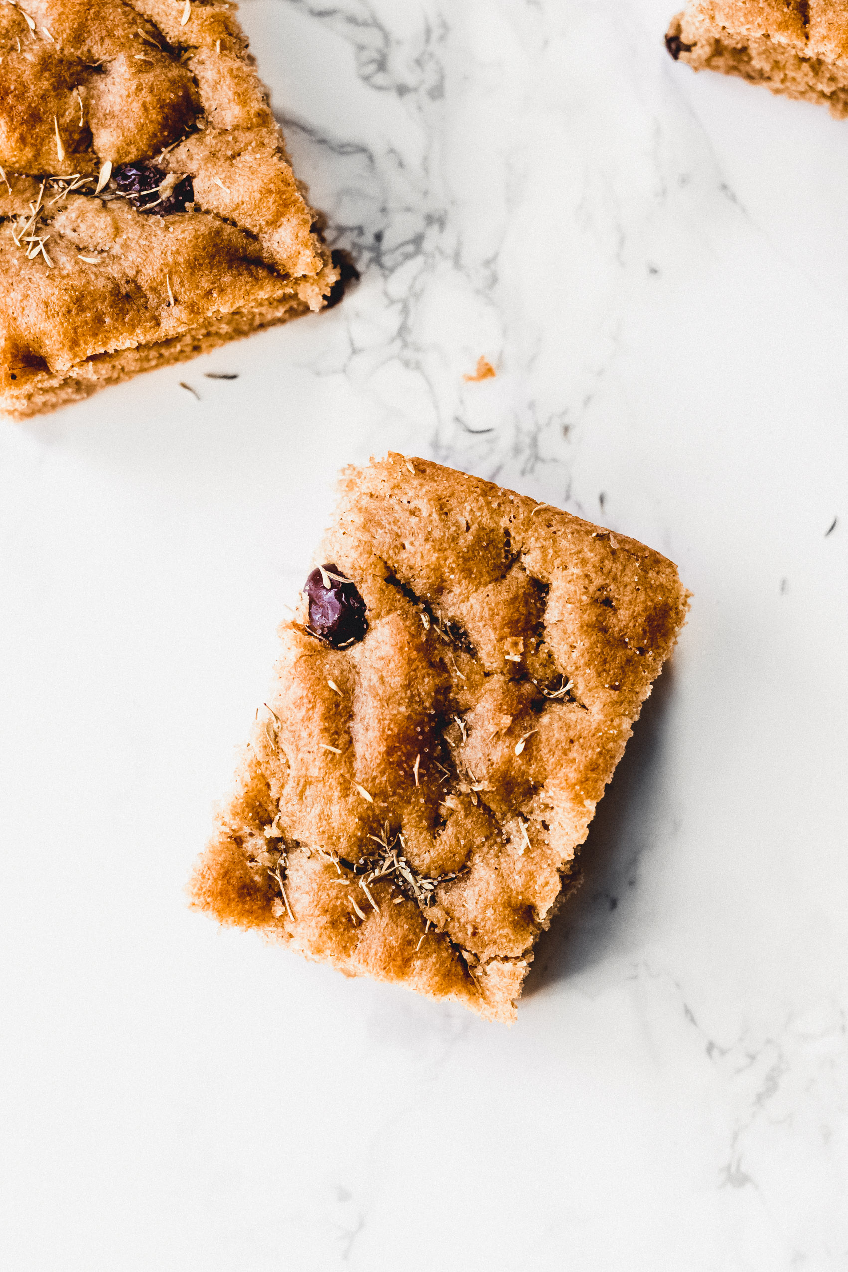 overhead image of brown square piece of focaccia with olives and rosemary