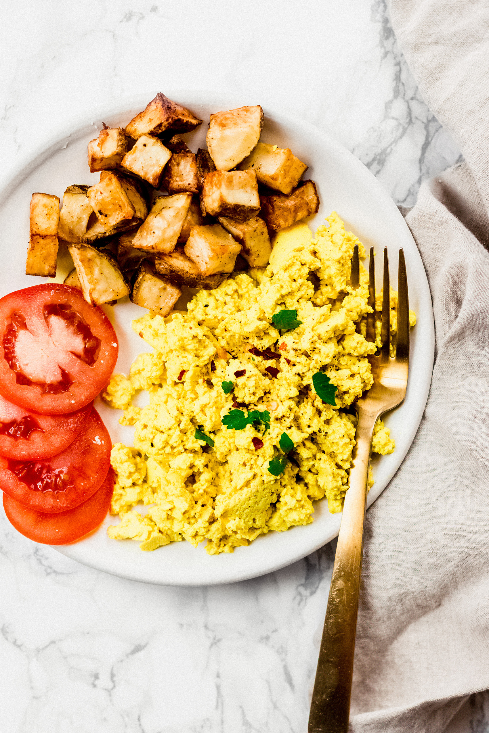 a plate of tofu scramble served with tomatoes and potatoes