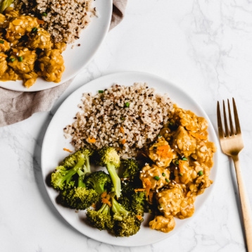 two plates of orange tempeh served alongside a scoop of quinoa and roasted broccoli
