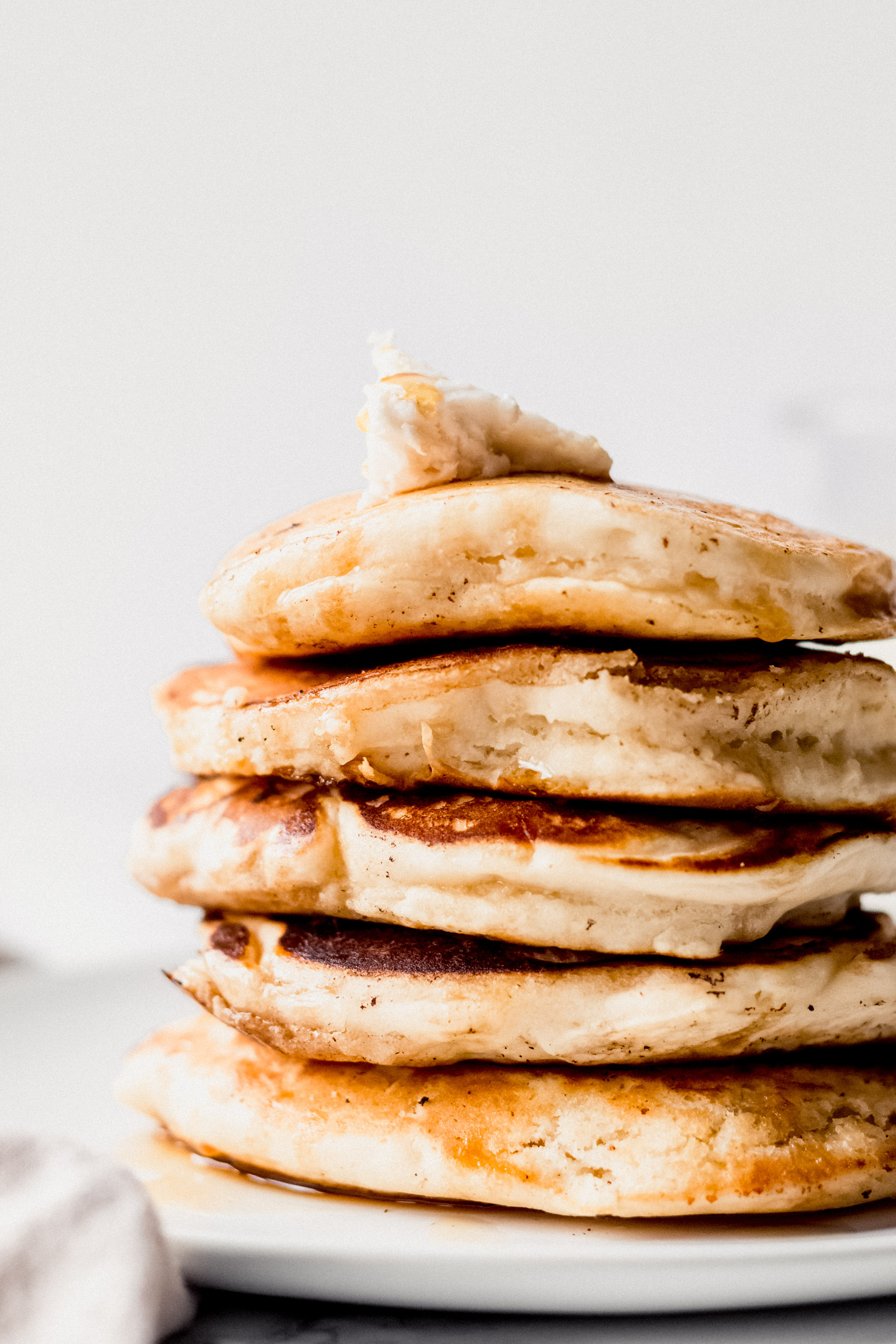 a closeup of a stack of five pancakes topped with vegan butter and maple syrup