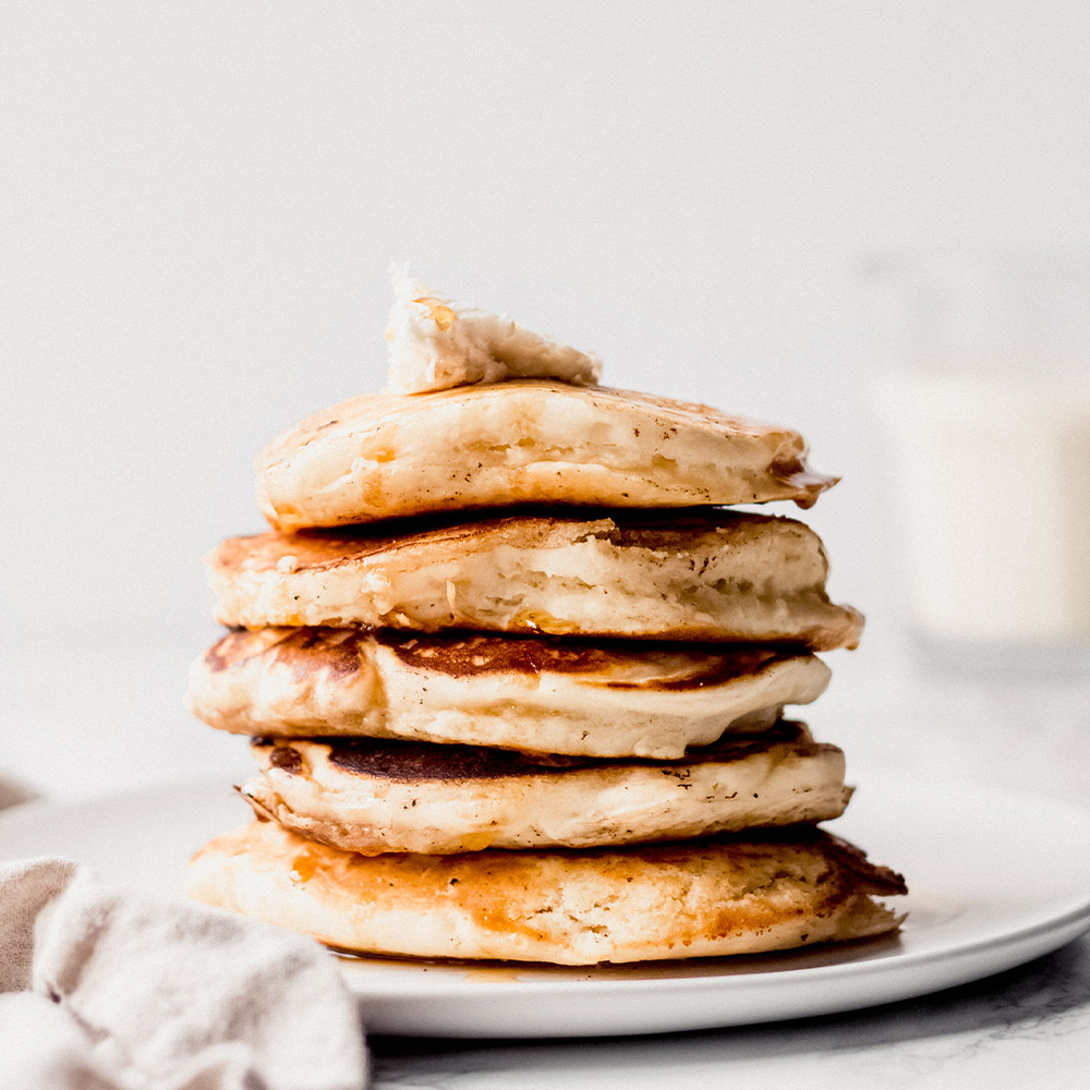 a stack of five classic pancakes topped with a pat of vegan butter